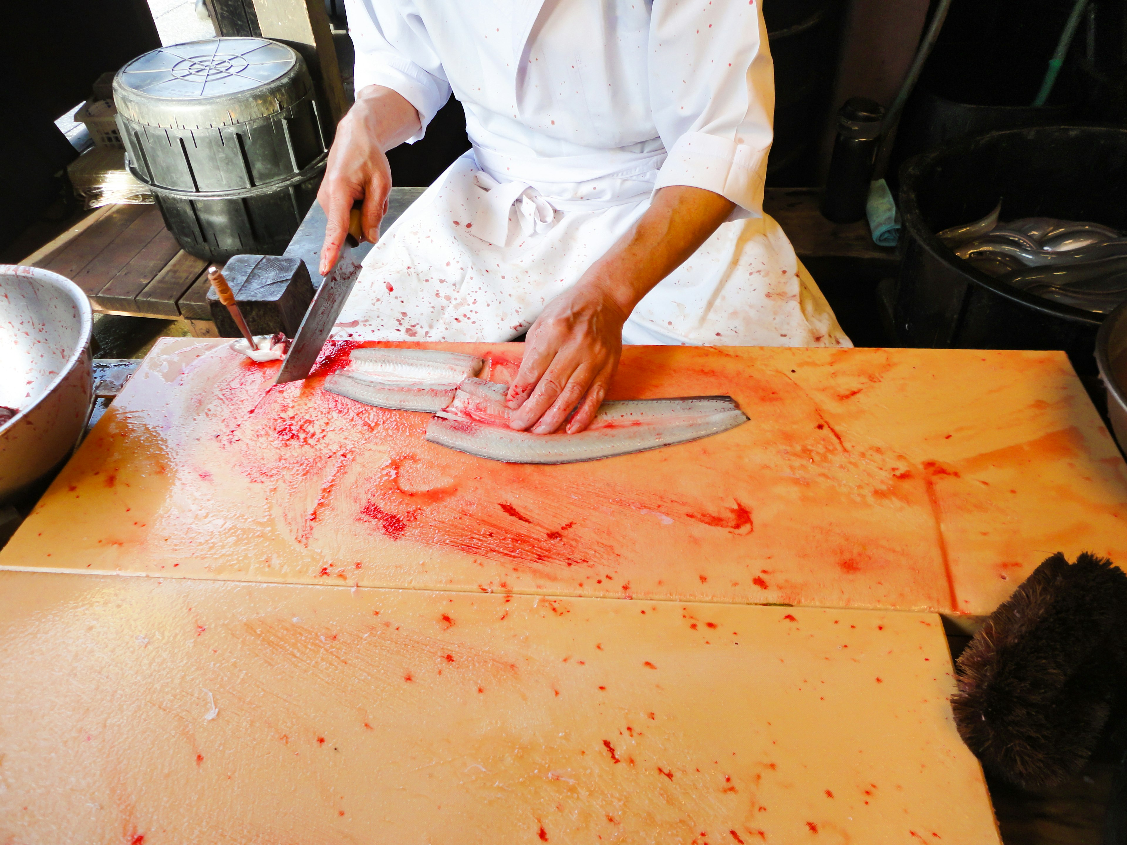 Chef découpant habilement un poisson sur une planche en bois avec des jus de poisson rouges vifs