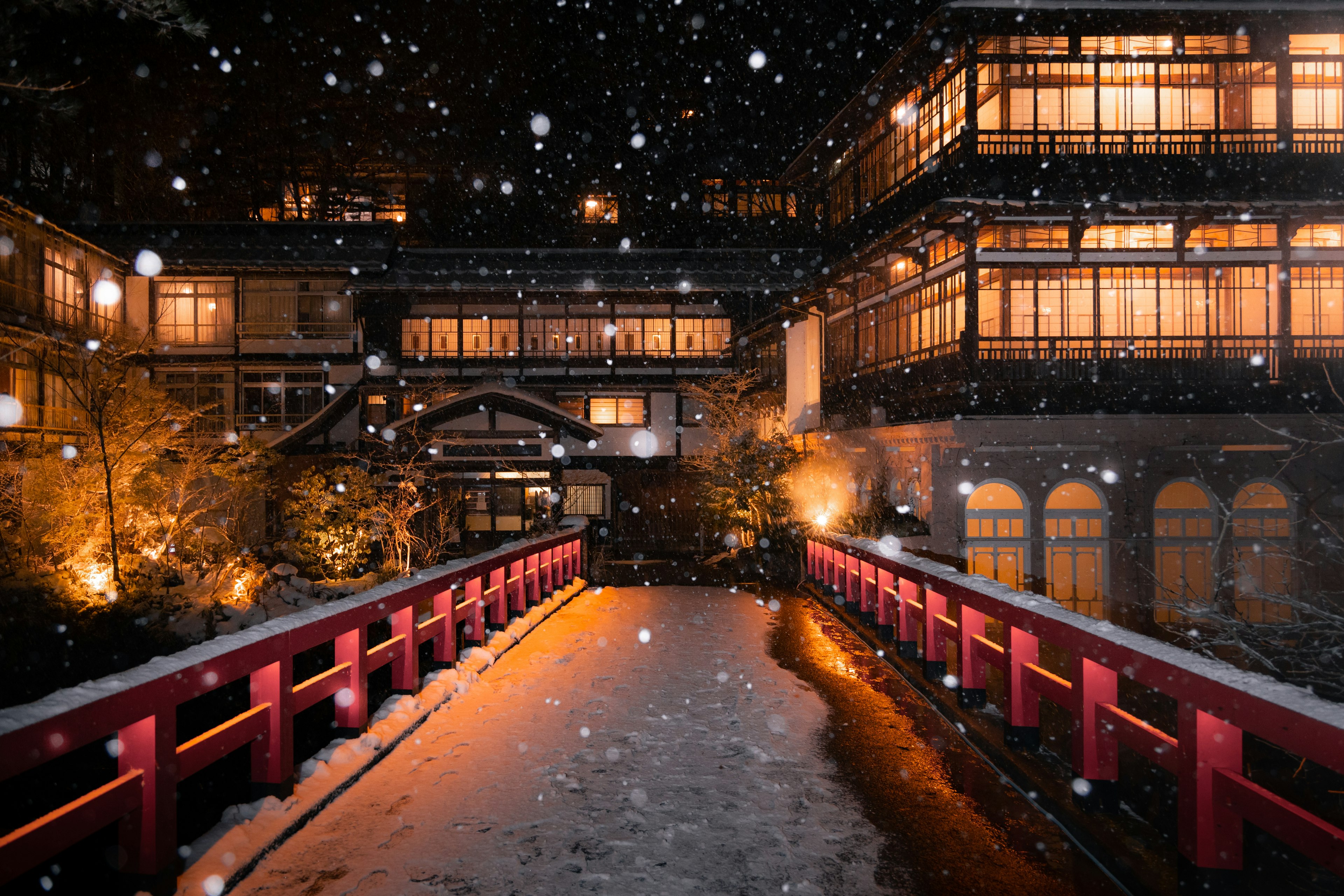 雪の中の赤い橋と伝統的な日本の宿泊施設の夜景