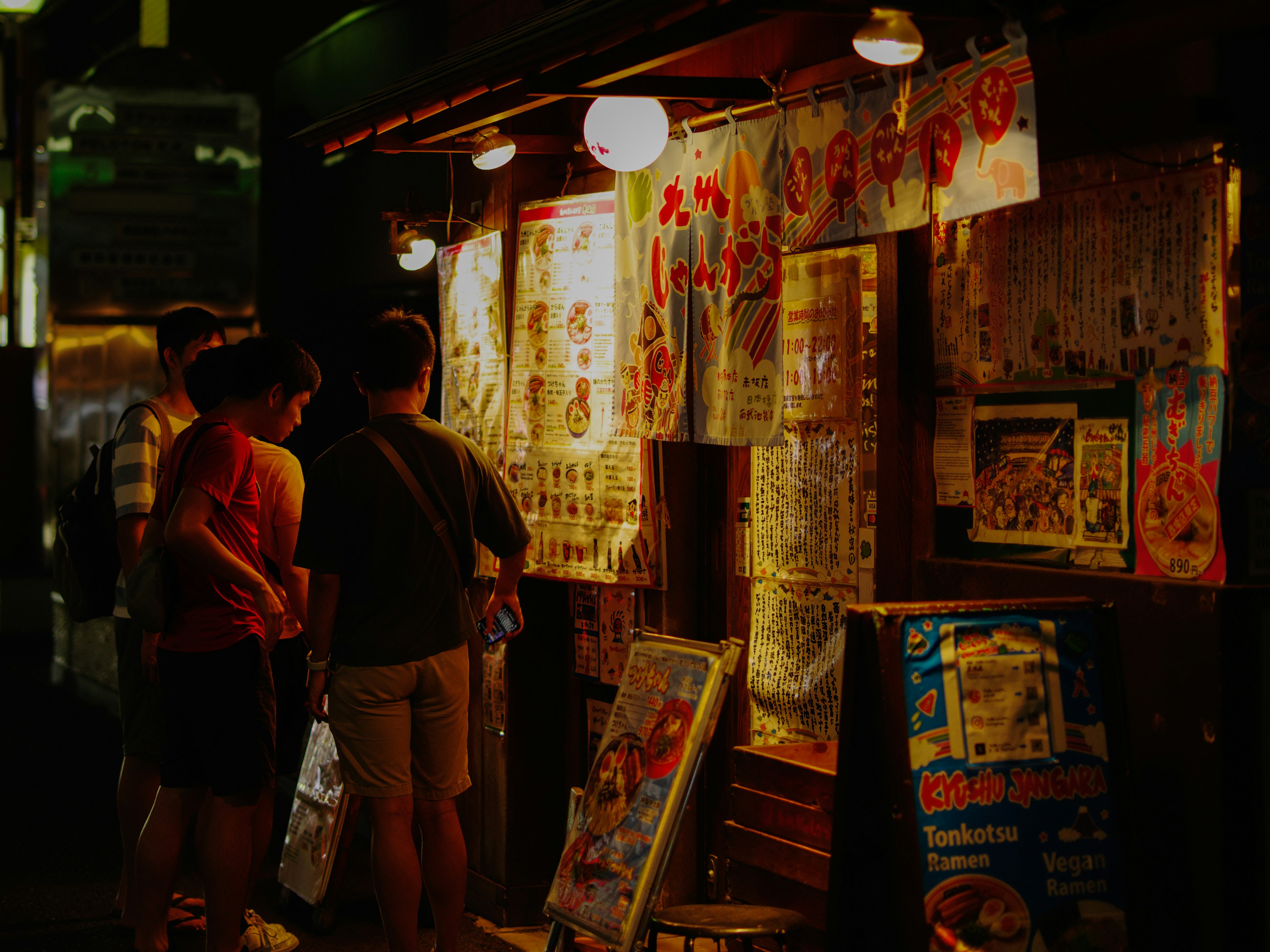 People looking at menus at a night market stall with bright lanterns