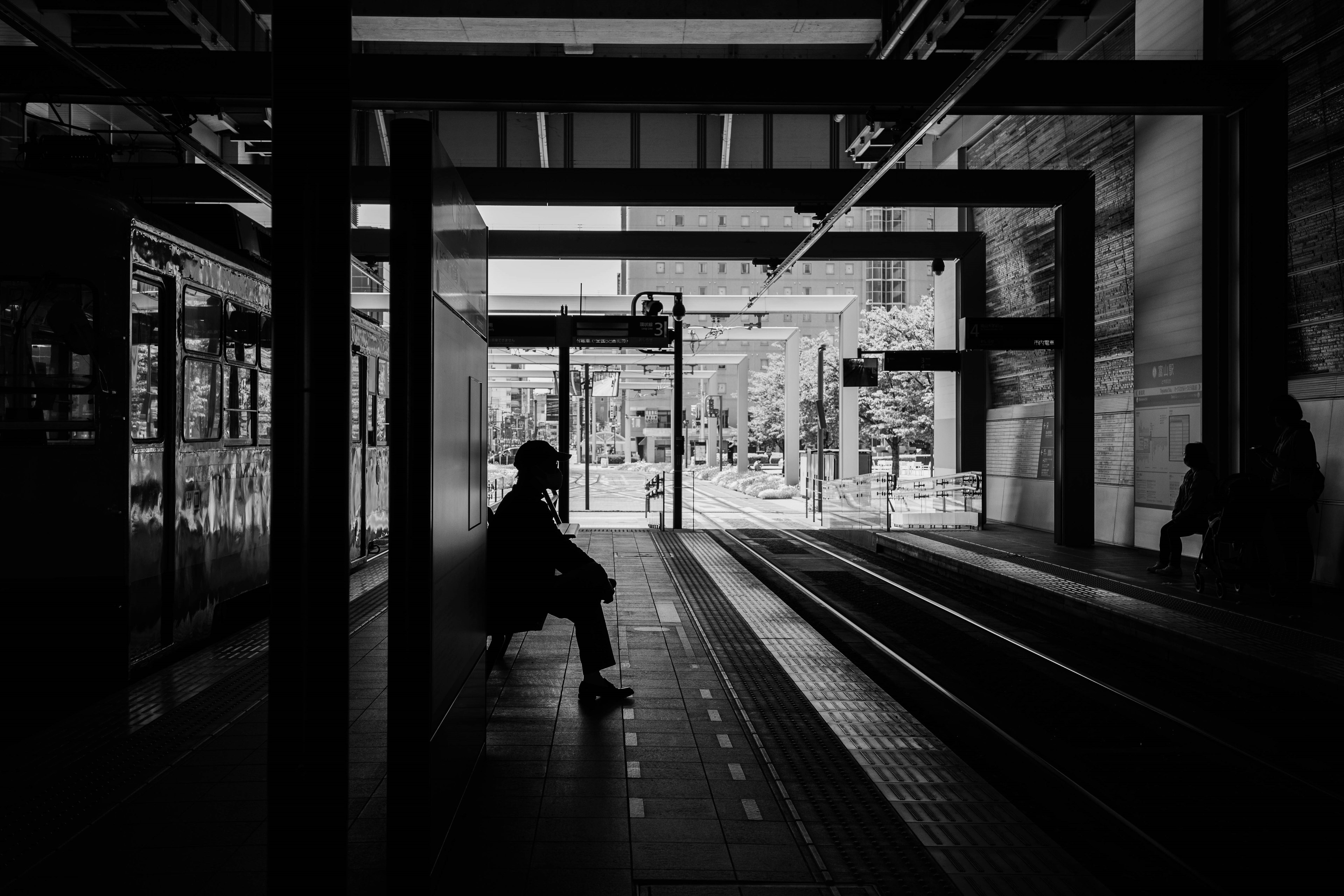 Silhouette einer Person, die auf einem Bahnsteig in einem Schwarz-Weiß-Bild sitzt