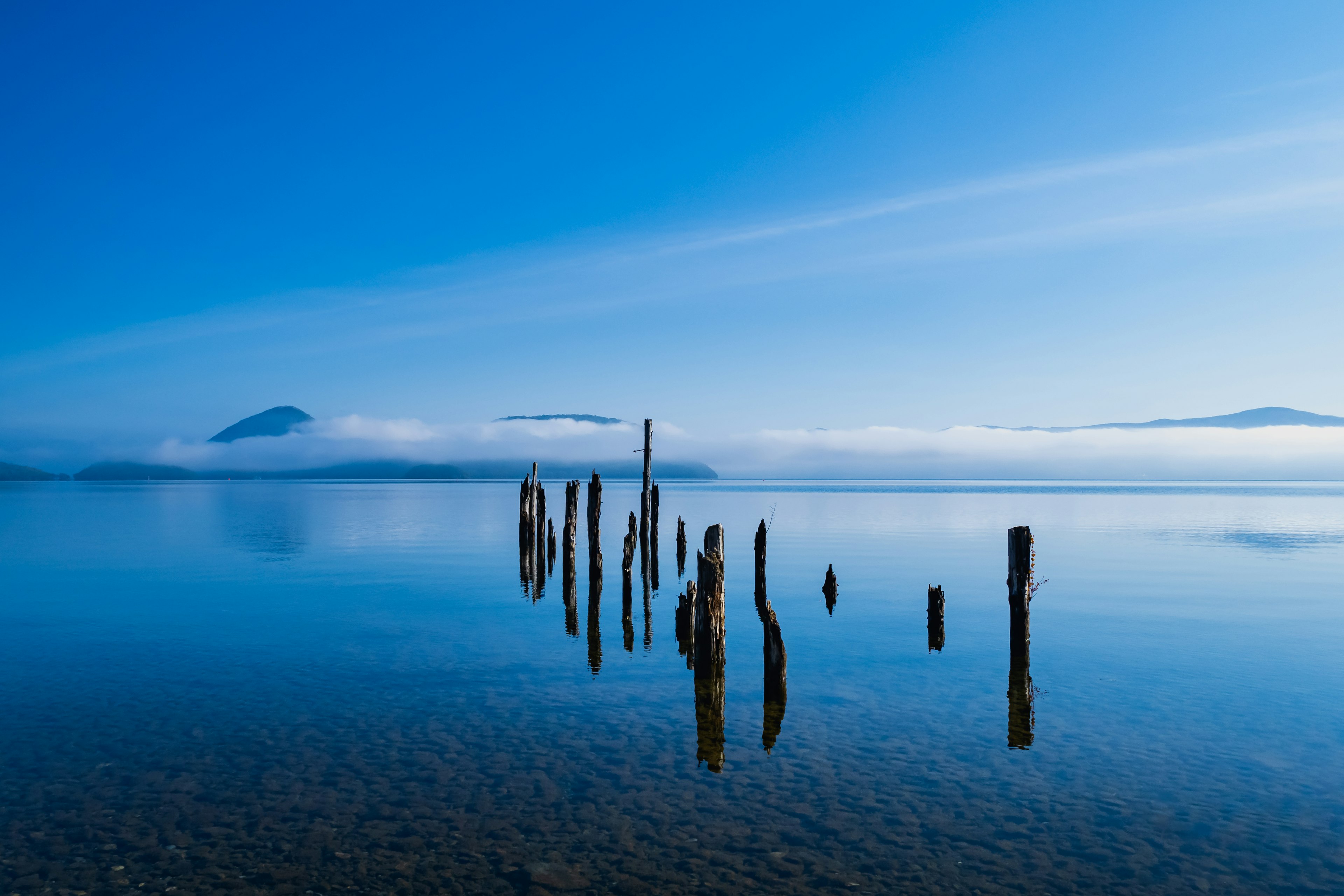 静かな湖面に立つ古い木の柱と青い空の風景