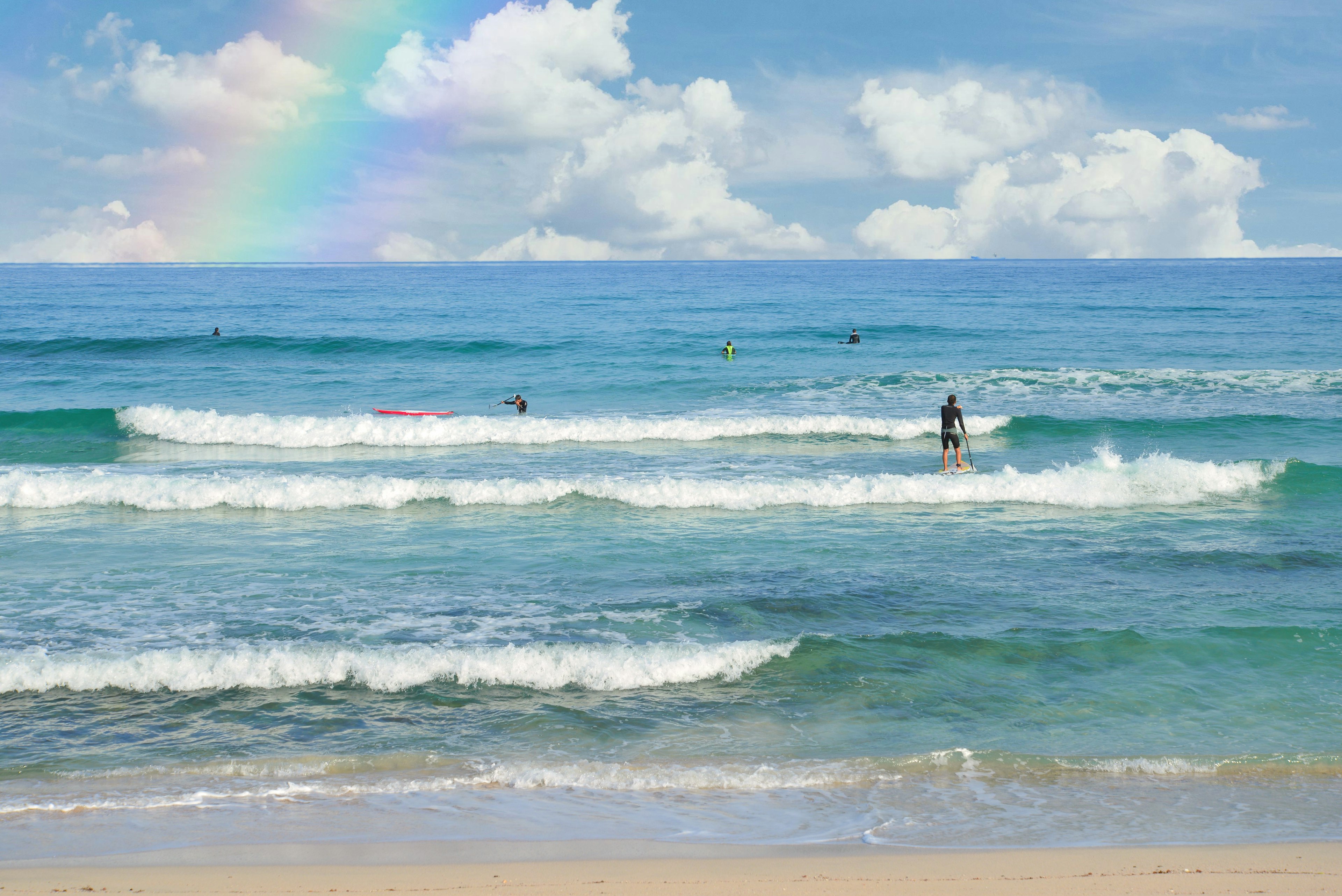 Vue pittoresque des vagues dans un océan bleu avec des surfeurs et un arc-en-ciel dans le ciel