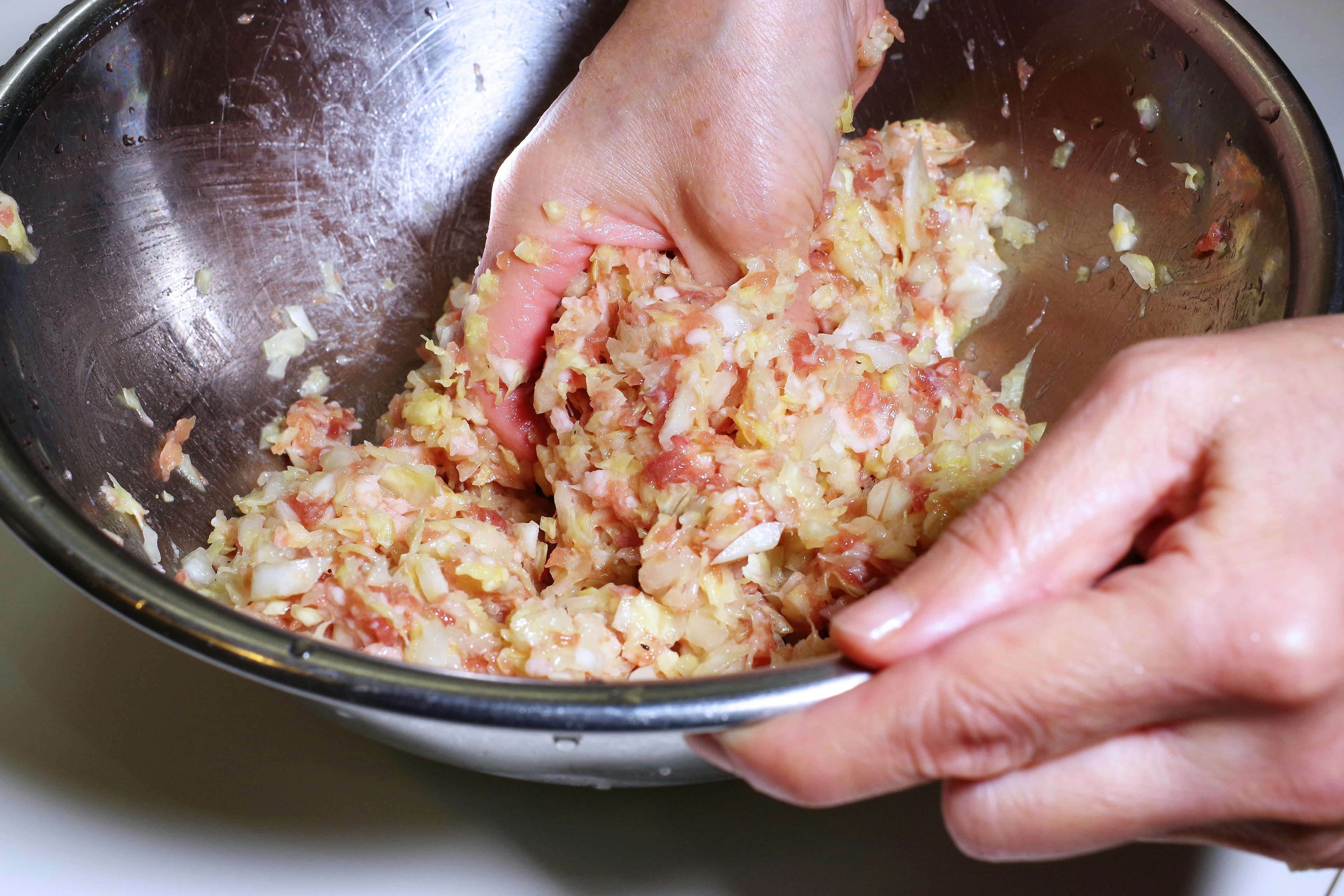 Hands mixing minced meat and vegetables in a bowl