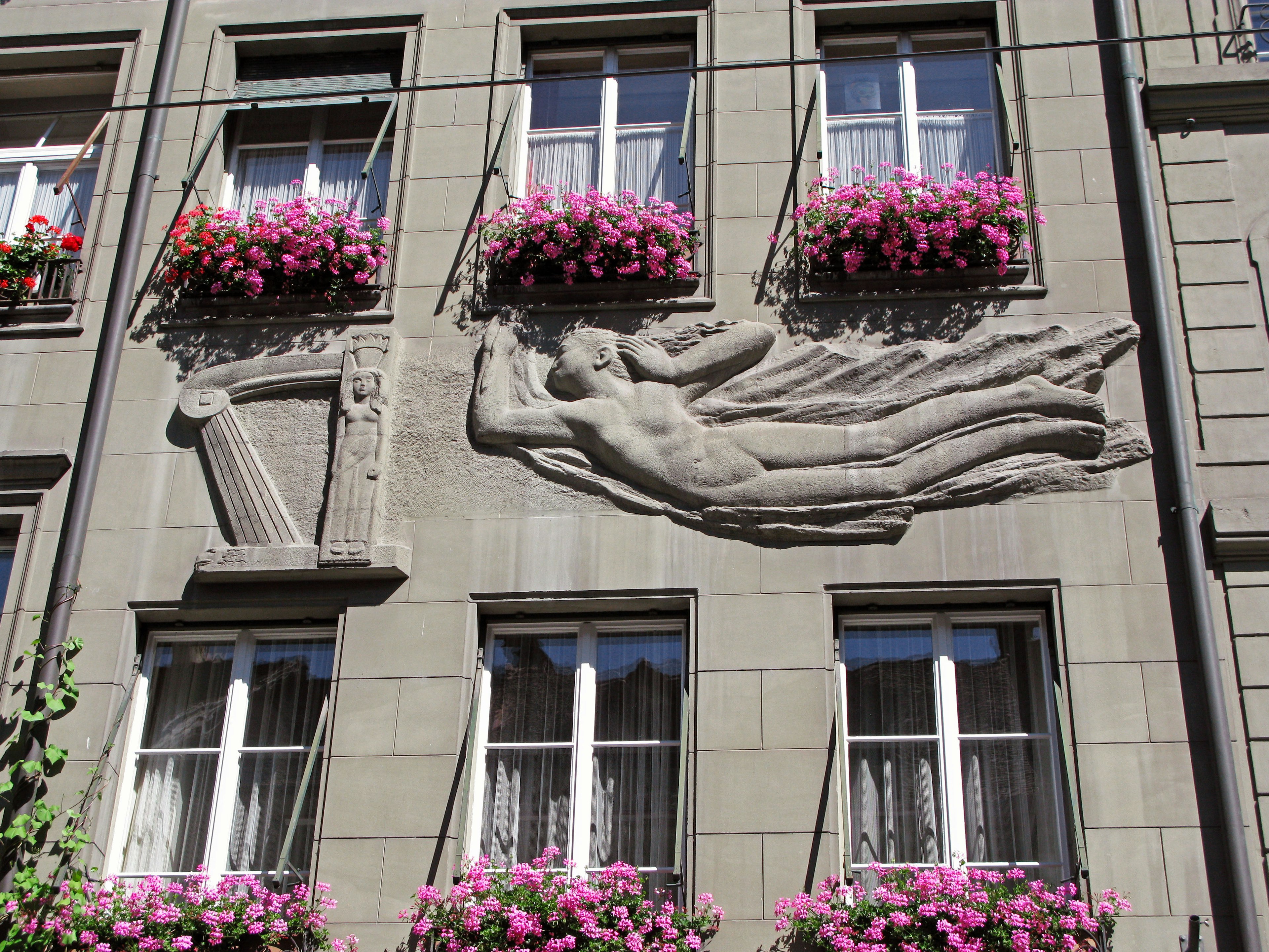 Scultura di una persona che fluttua su un muro di edificio con cesti di fiori colorati