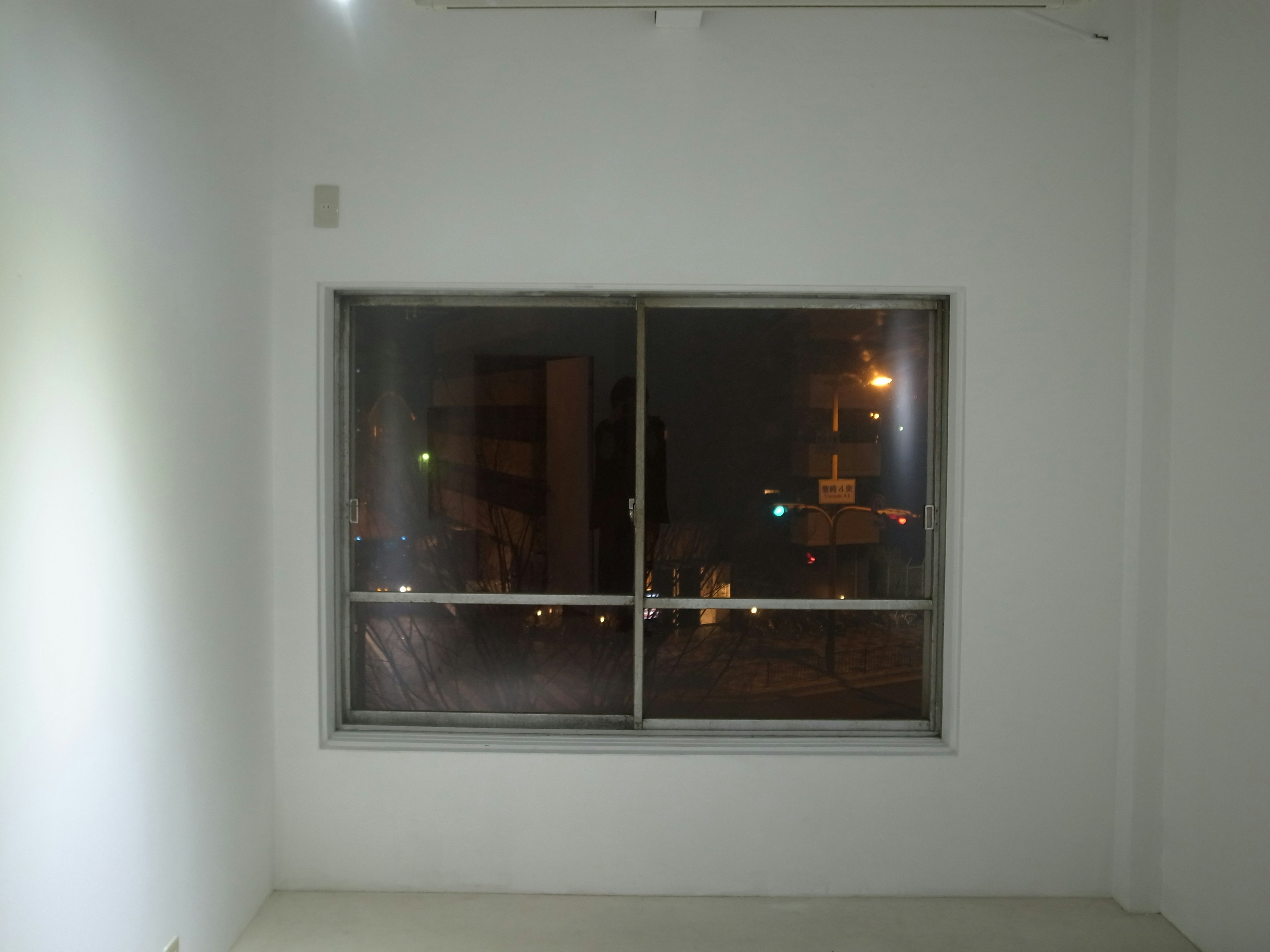 A window in a white room reflecting city lights at night