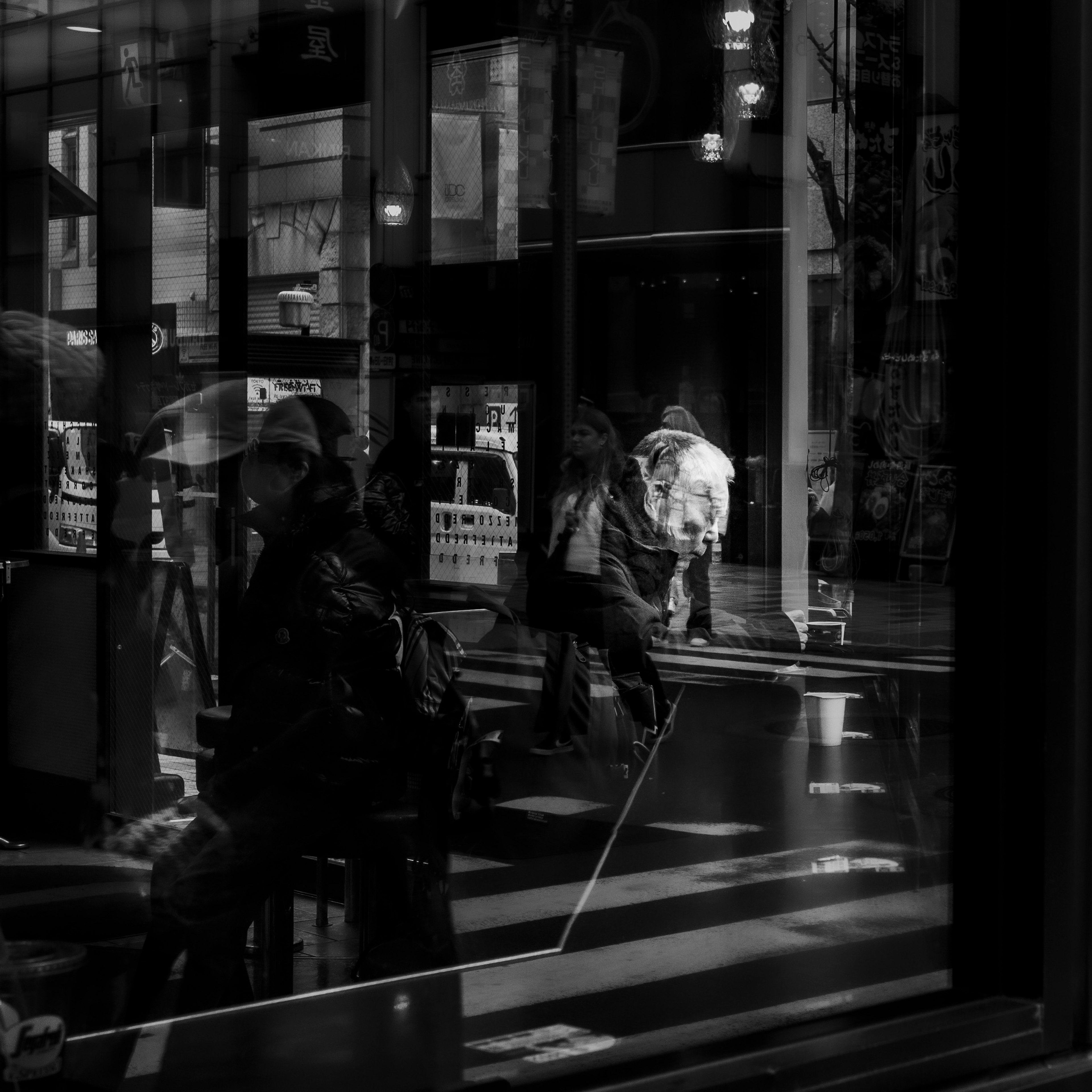 Escena urbana en blanco y negro con reflejos de personas que pasan por el vidrio