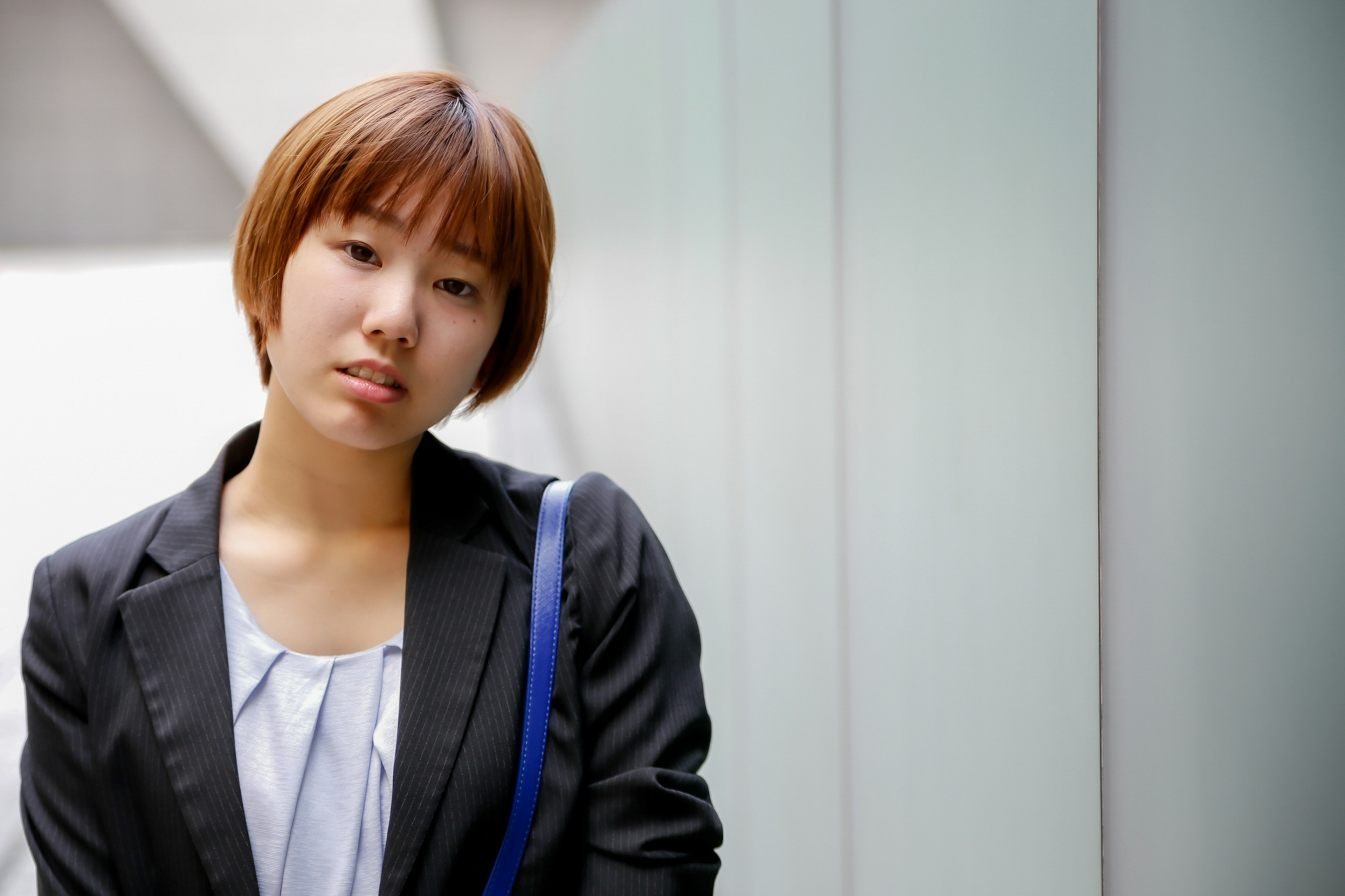 A short-haired woman wearing a suit with a modern building wall in the background