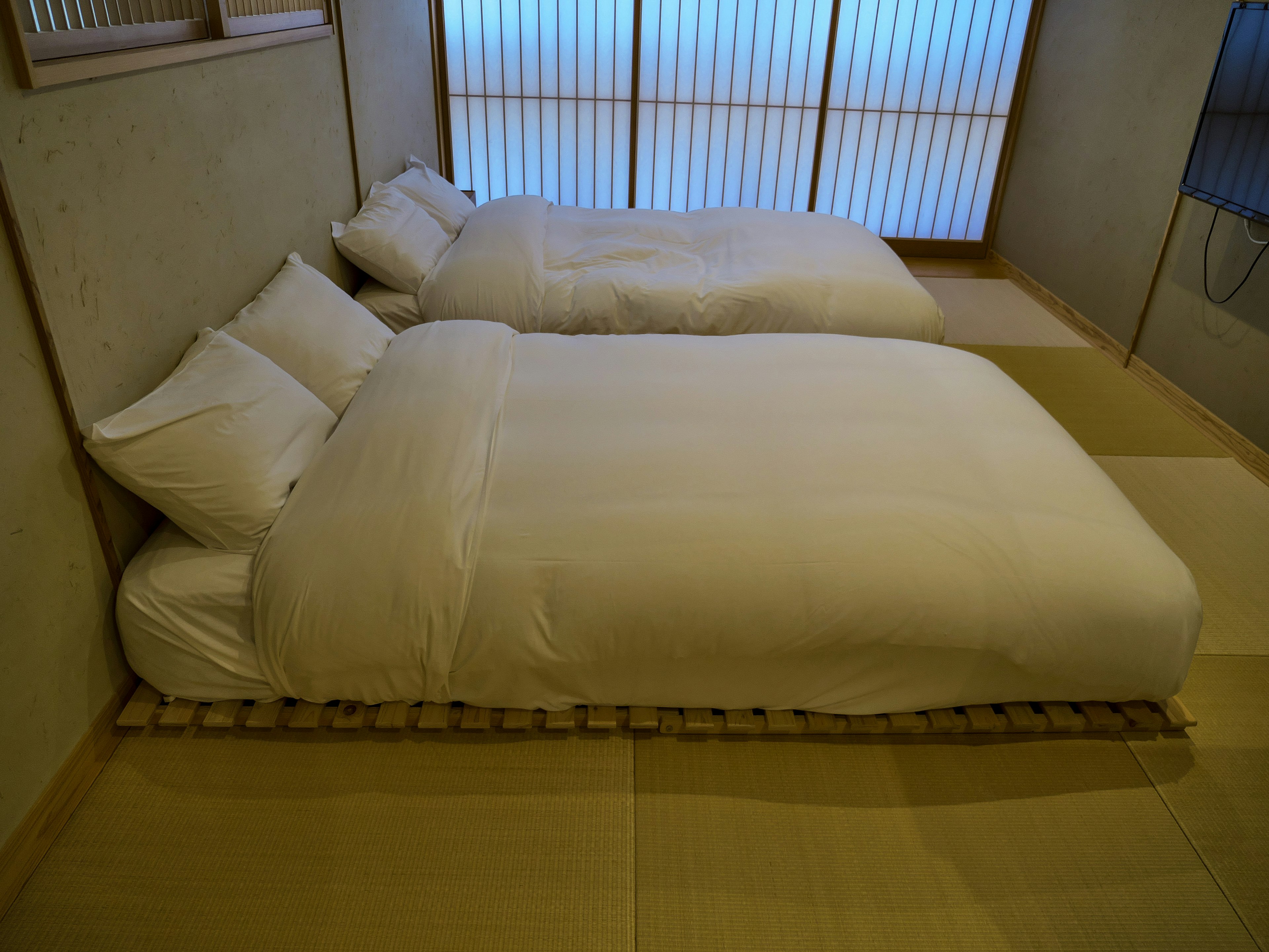 Deux futons blancs disposés dans une chambre de style japonais avec un sol en tatami