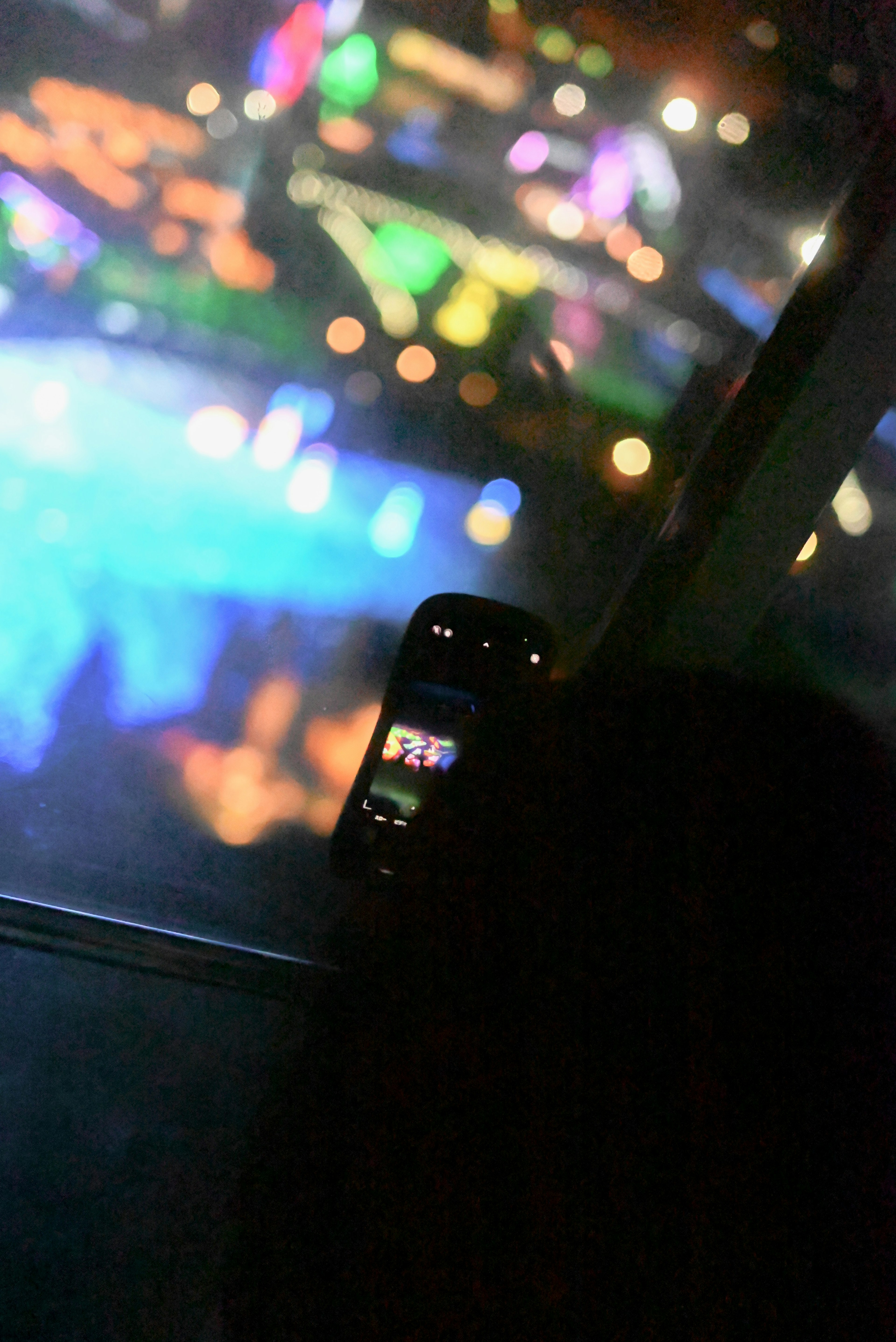 Photo d'une personne près d'une fenêtre prenant des photos des lumières de la ville avec un téléphone mobile reflets colorés en arrière-plan