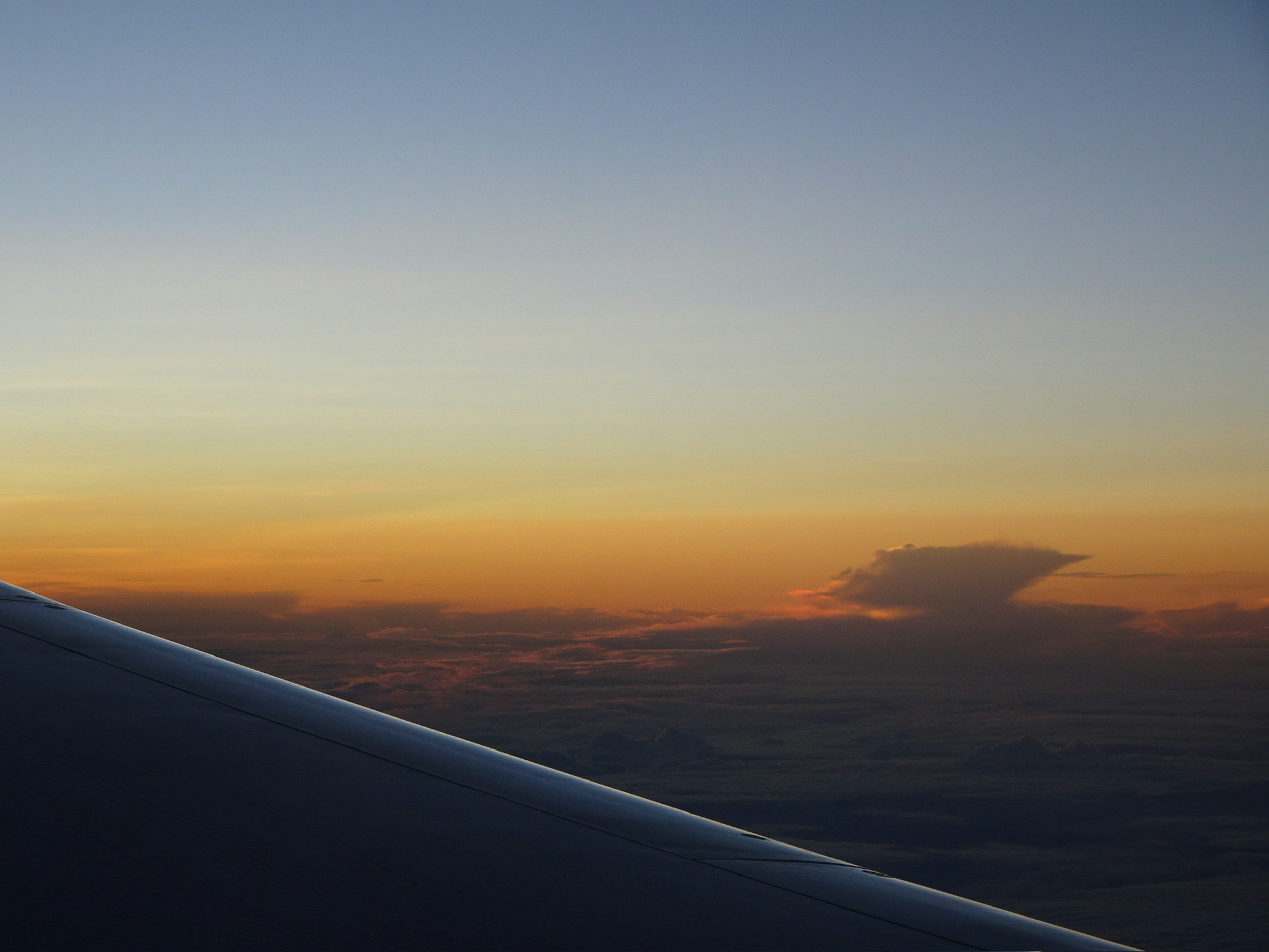 Airplane wing with a silhouette of clouds and a sunset sky