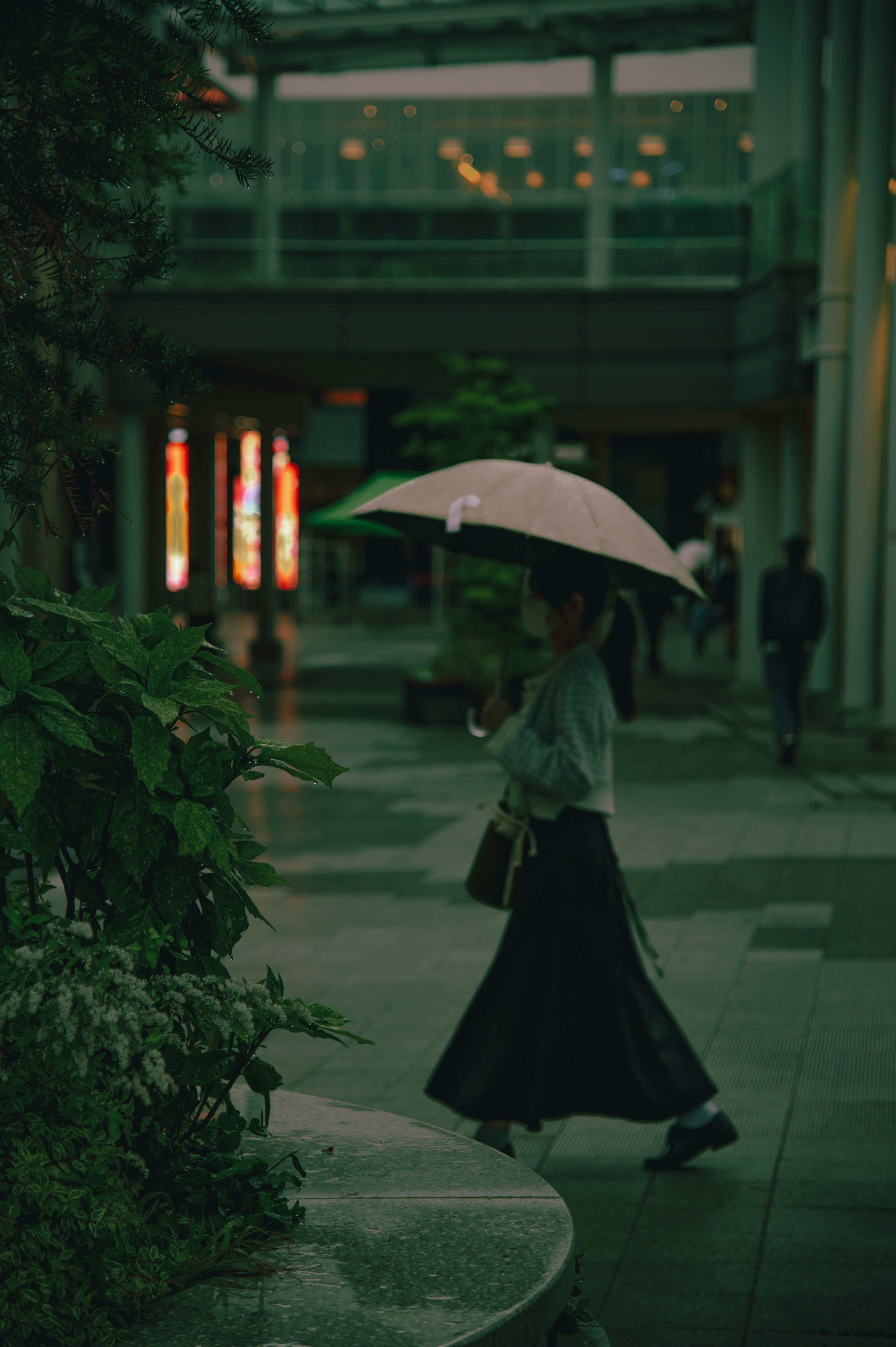 Mujer caminando con un paraguas en un entorno urbano débilmente iluminado