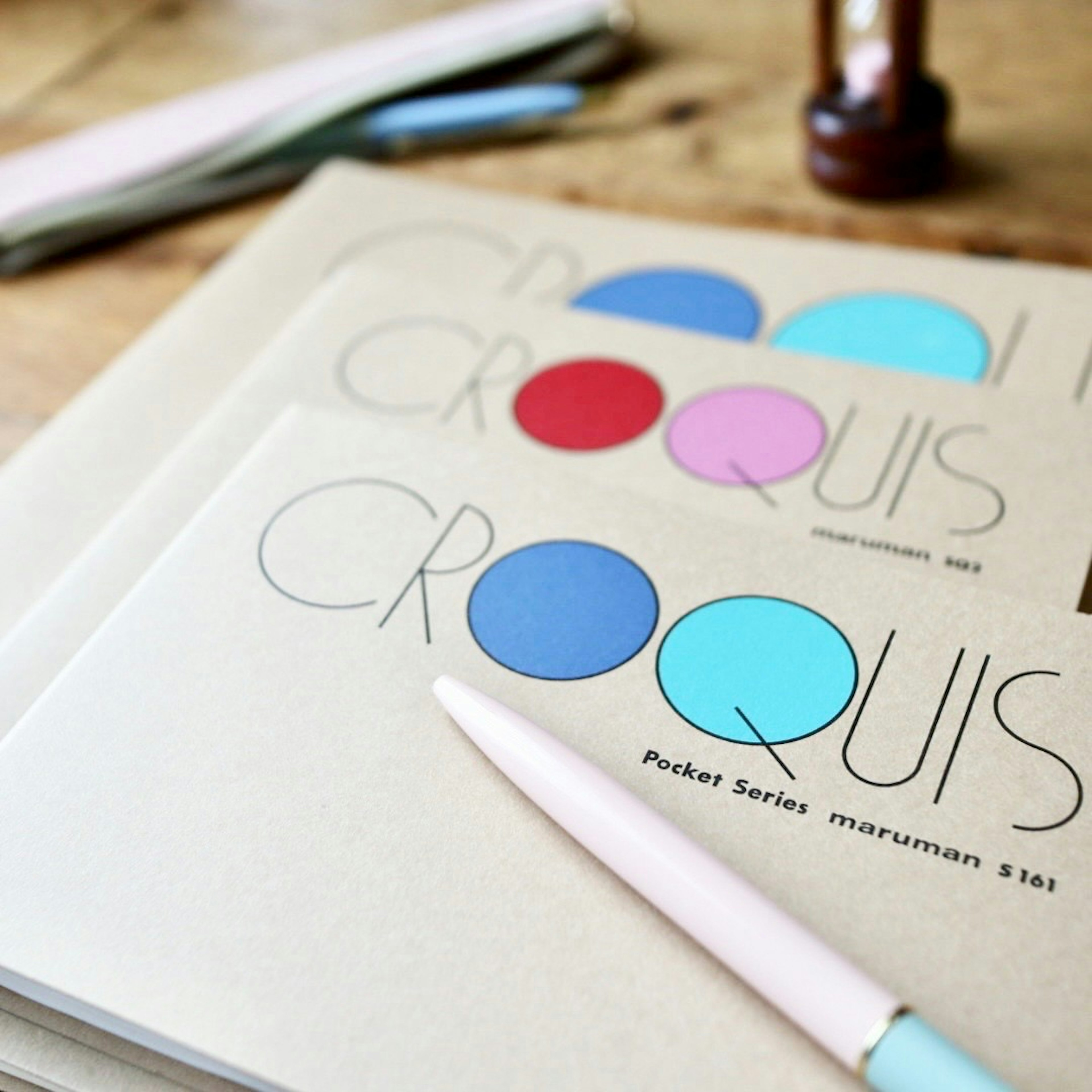 Sketchbooks with colorful circles and a pastel pen on a wooden table