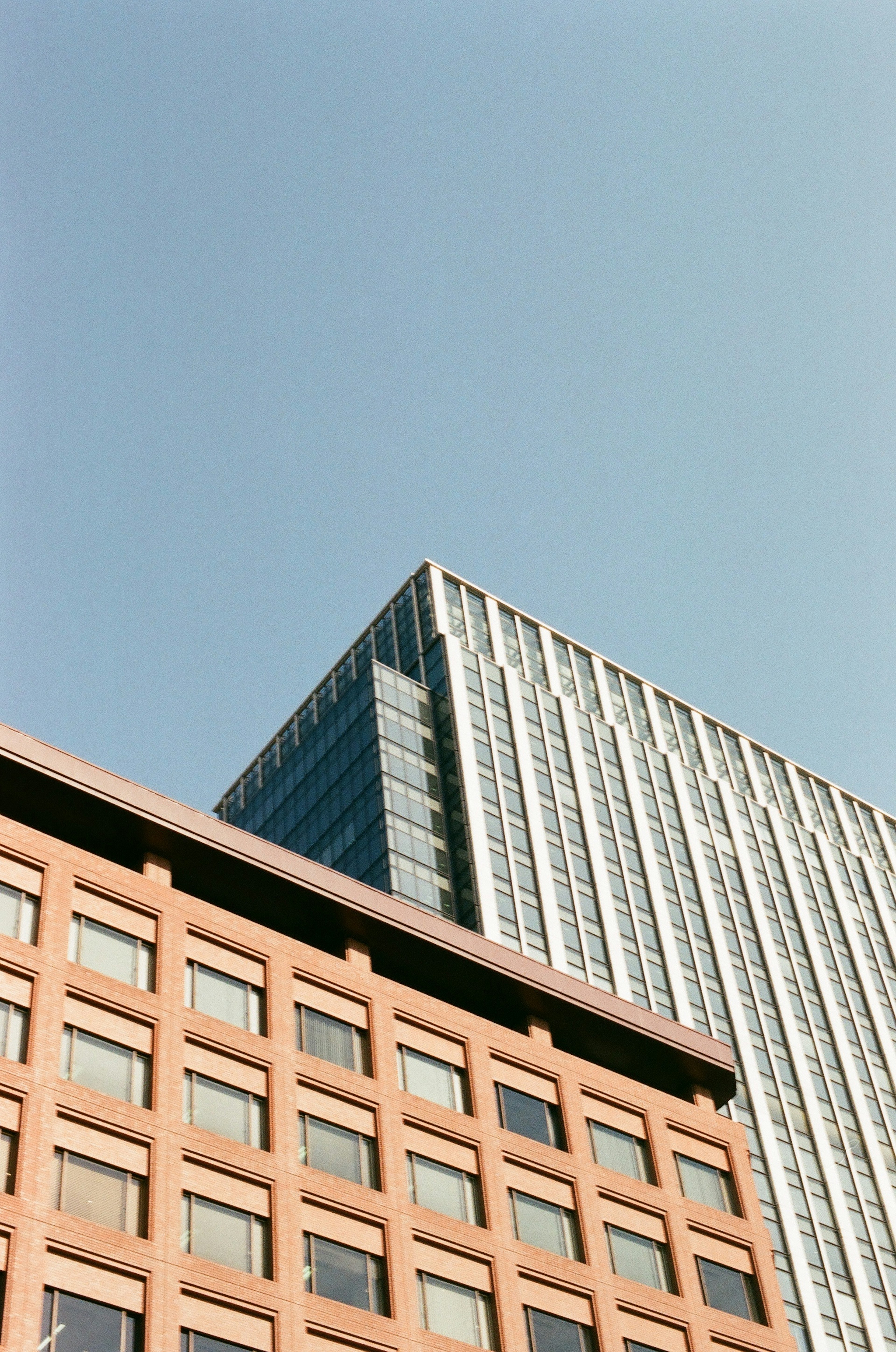 Modern glass building and classic brick structure against a clear blue sky