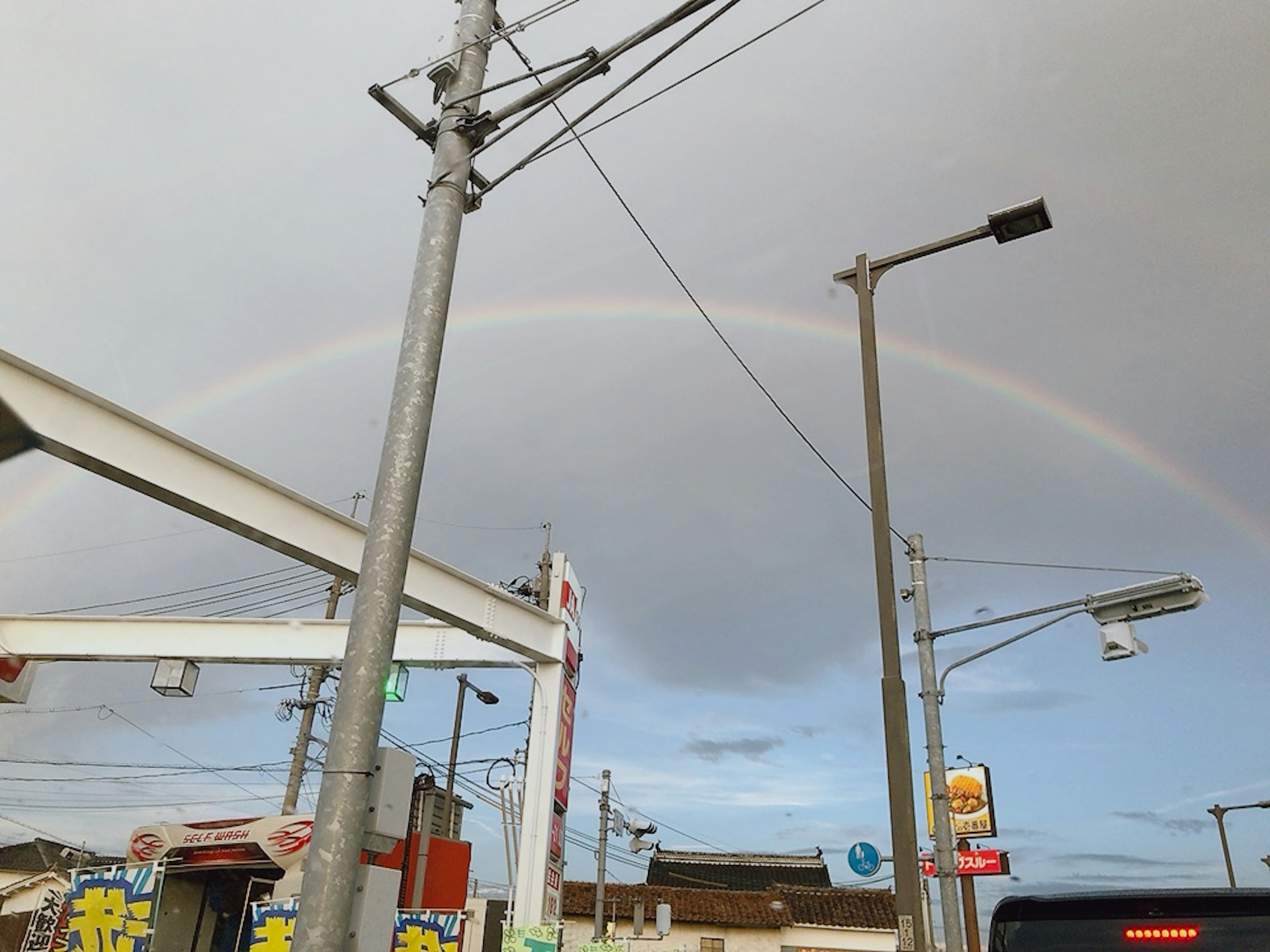 Arco iris sobre un cielo nublado con paisaje urbano y líneas eléctricas