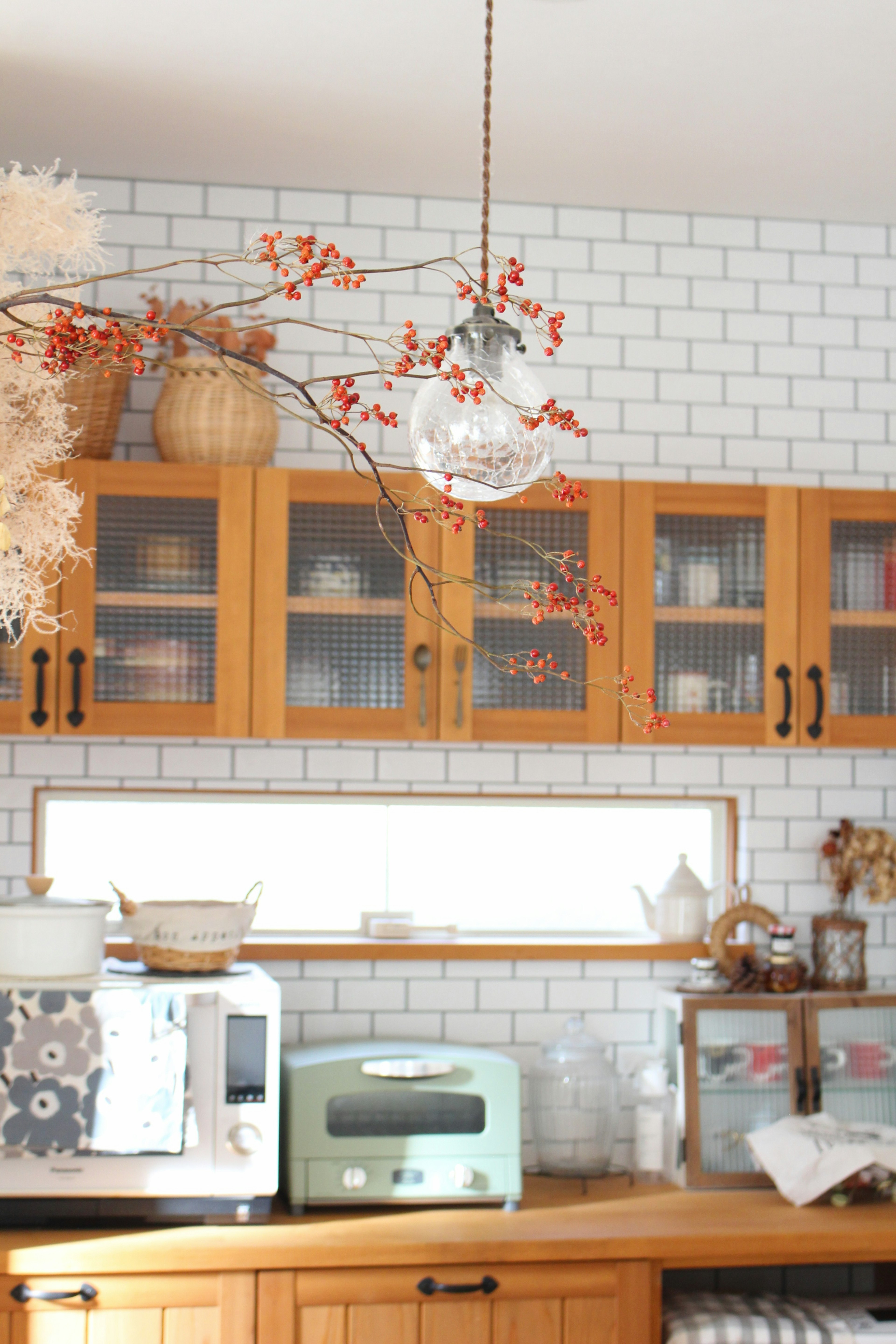 Interior de cocina brillante con gabinetes de madera pared de azulejos blancos iluminación decorativa y ramas de otoño