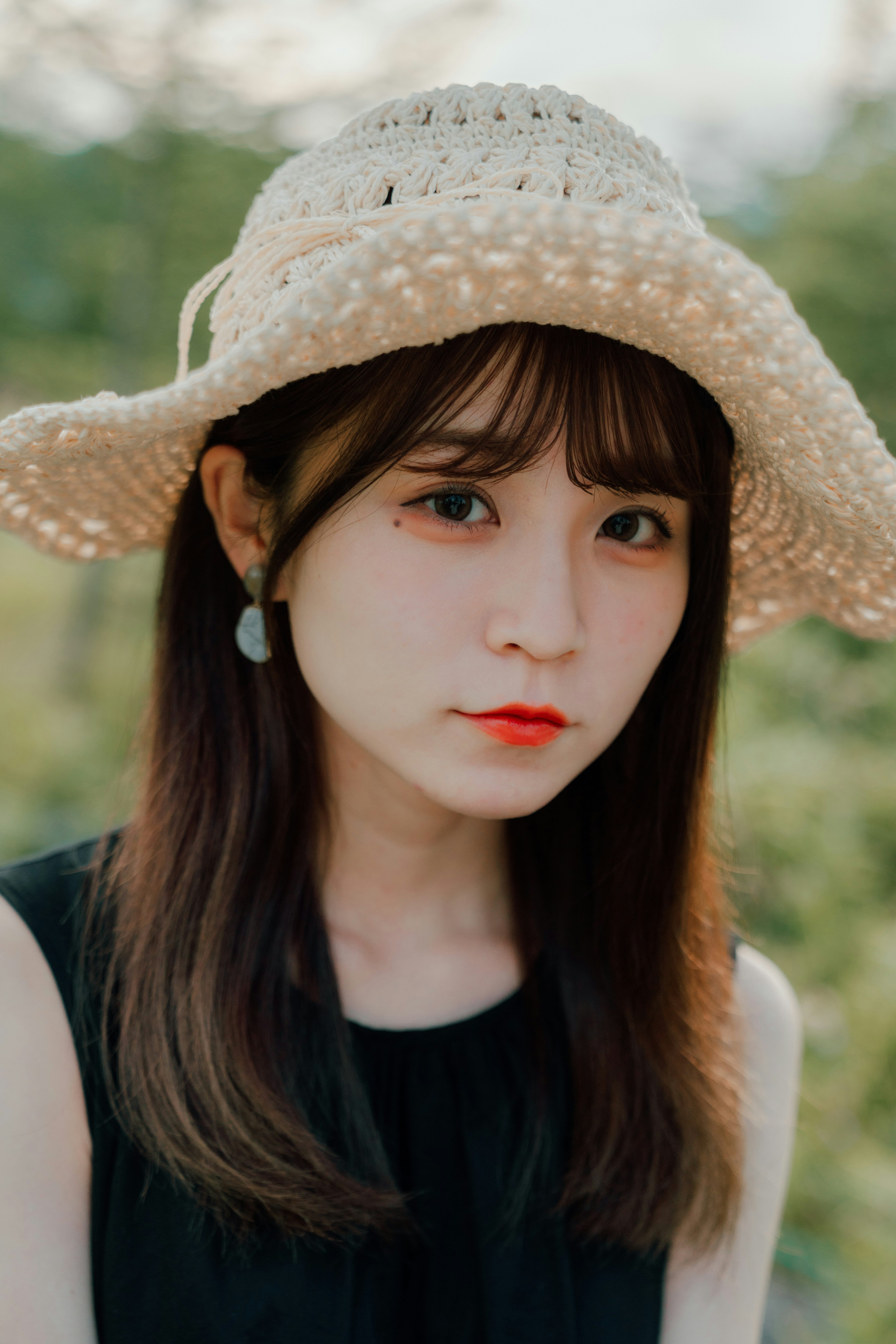 Portrait of a woman wearing a straw hat dressed in black with a green natural background