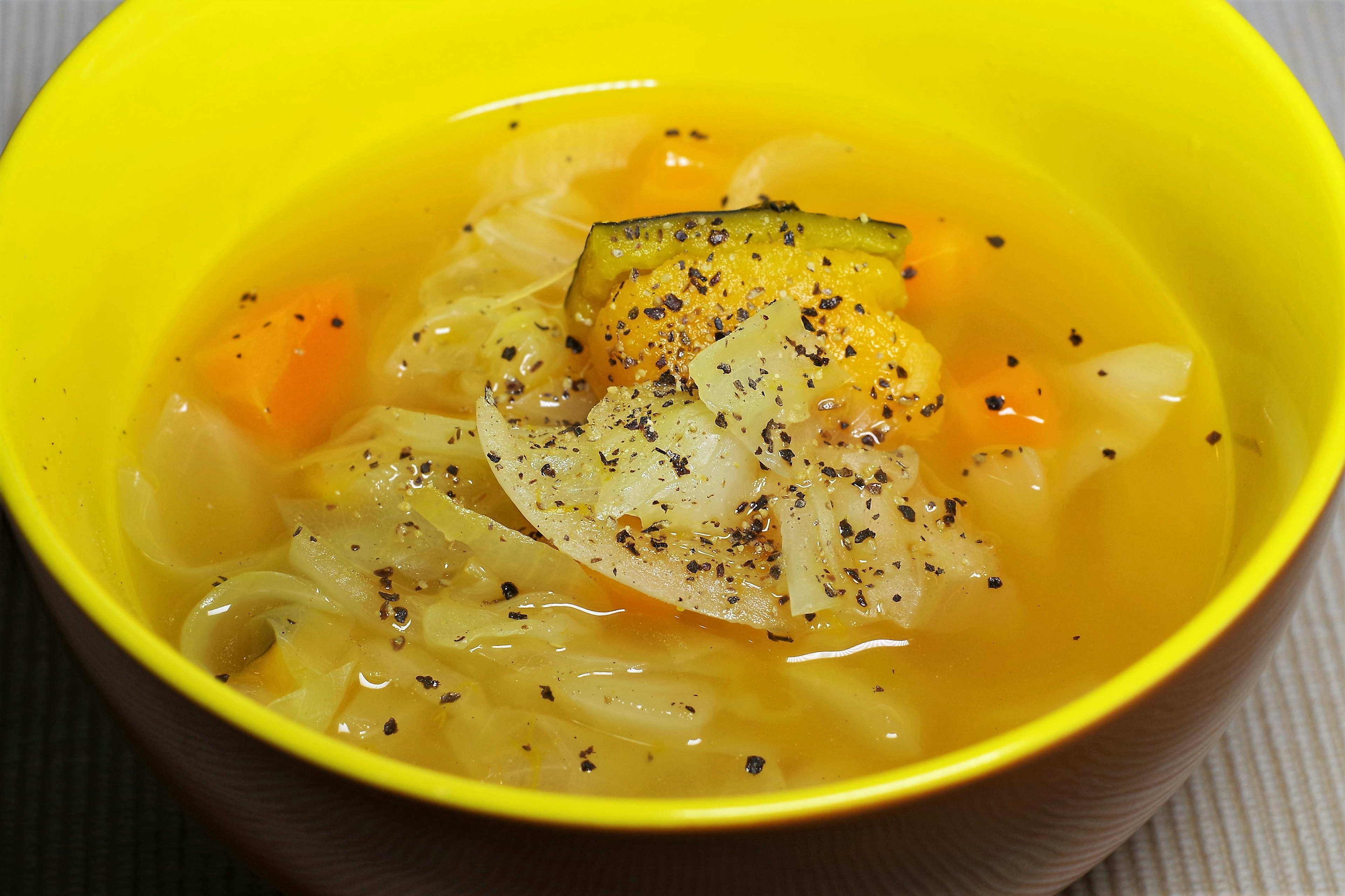 Image of vegetable soup in a yellow bowl featuring cabbage, carrots, and spices