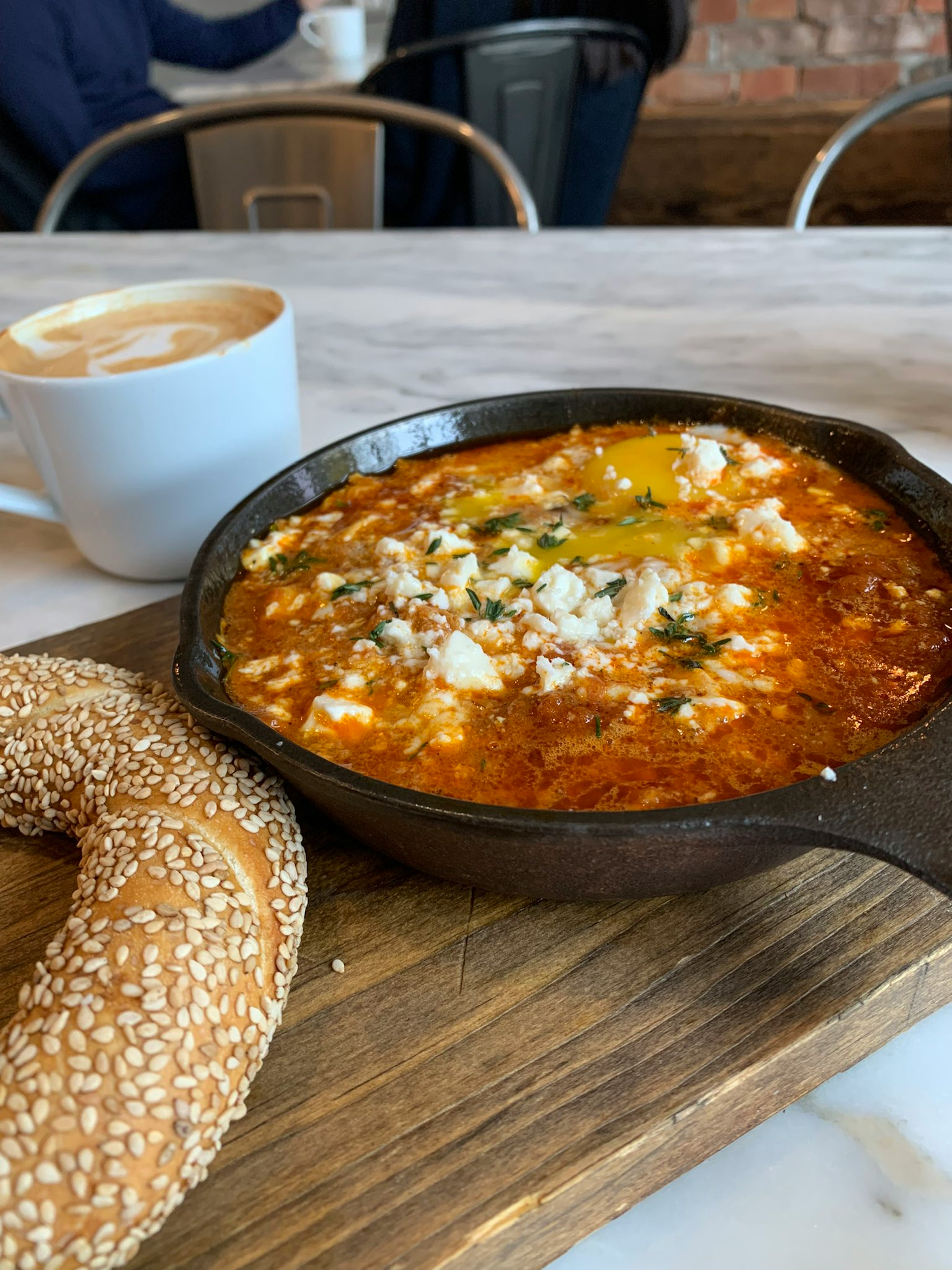 Skillet dish with feta cheese and herbs alongside a sesame bagel and coffee