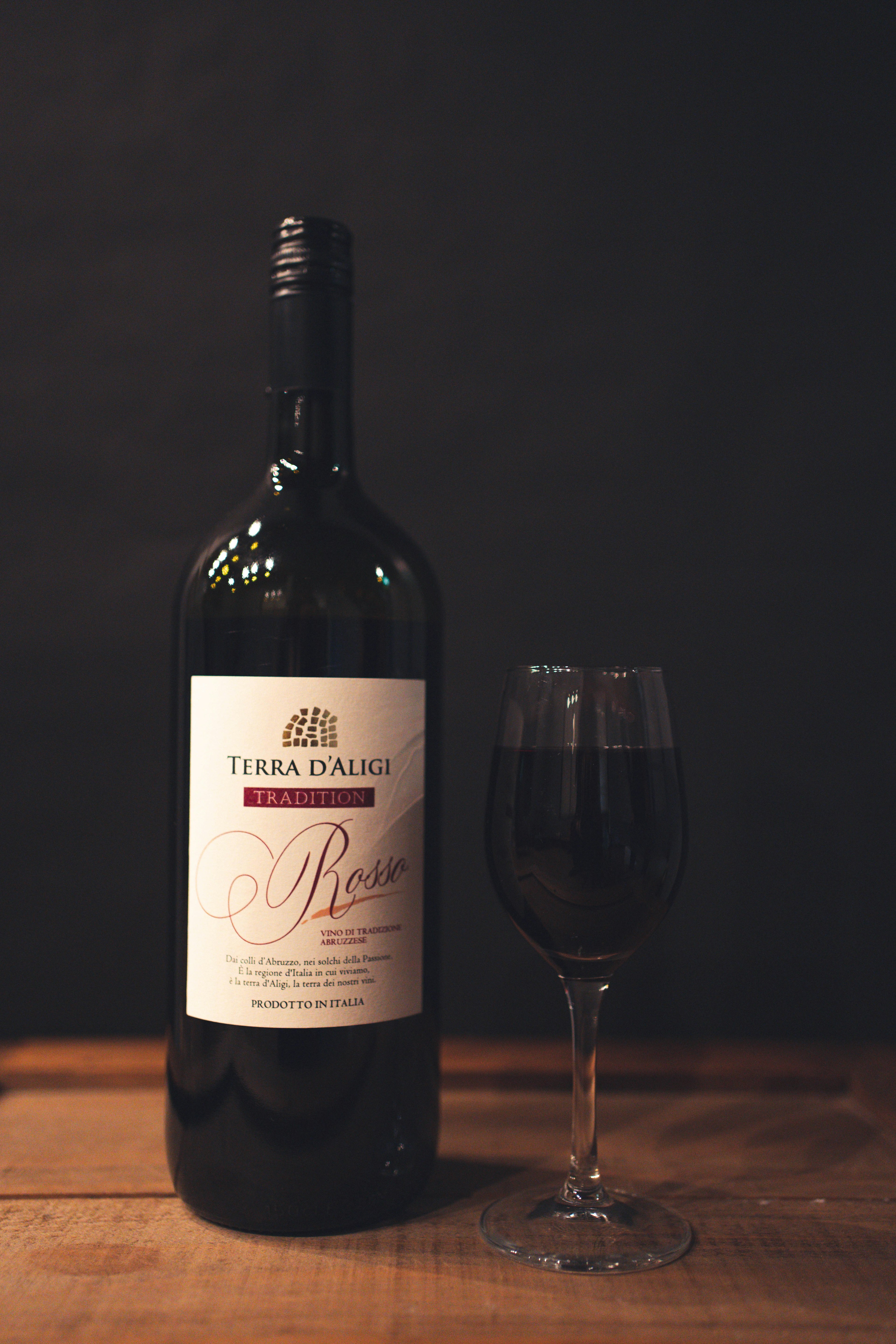 A bottle of red wine and a glass placed on a wooden table