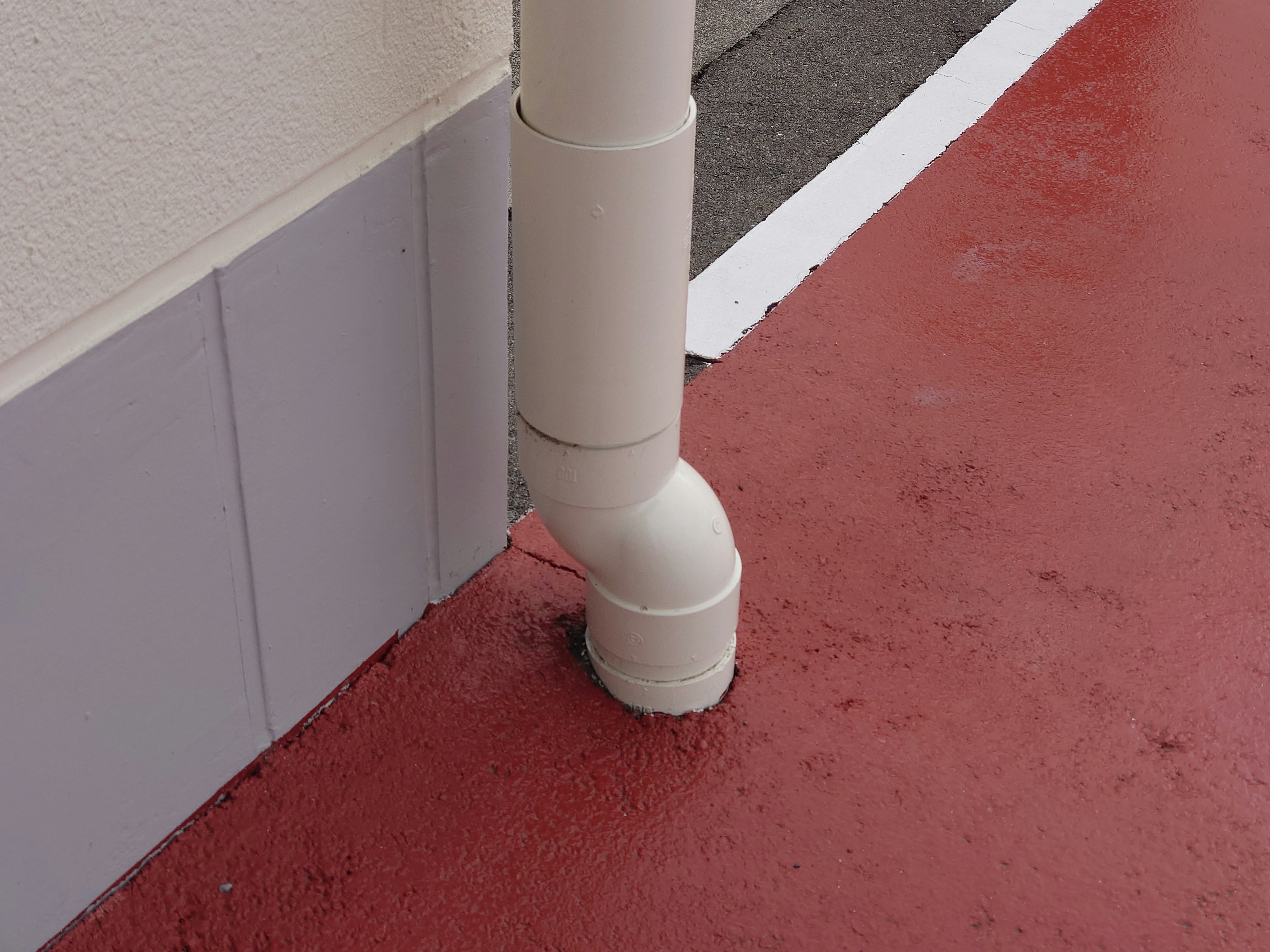 White drainage pipe at the corner of a red floor