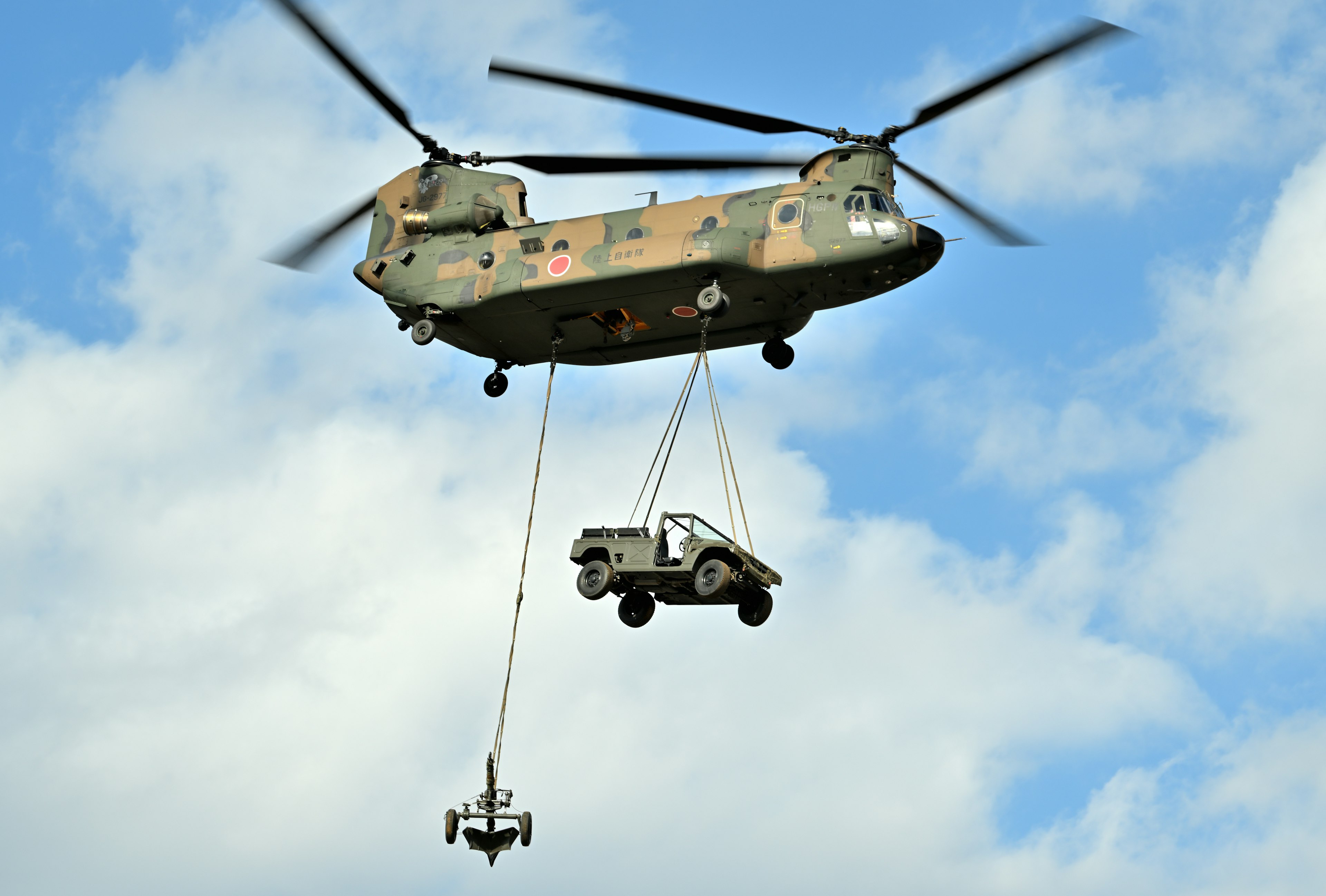 Military helicopter lifting vehicle with cargo hook in flight