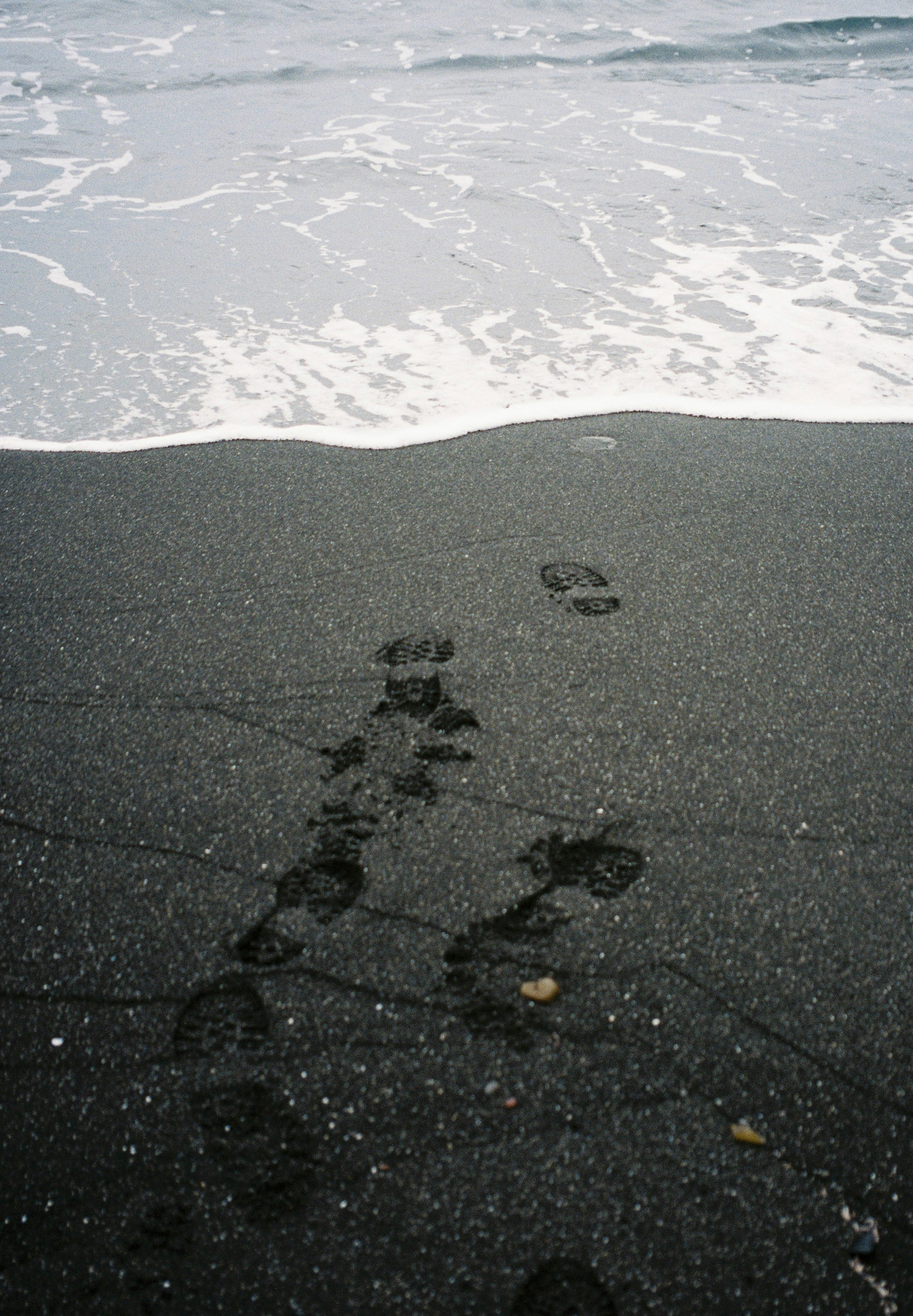 Fußabdrücke an einem schwarzen Sandstrand nahe der Küste