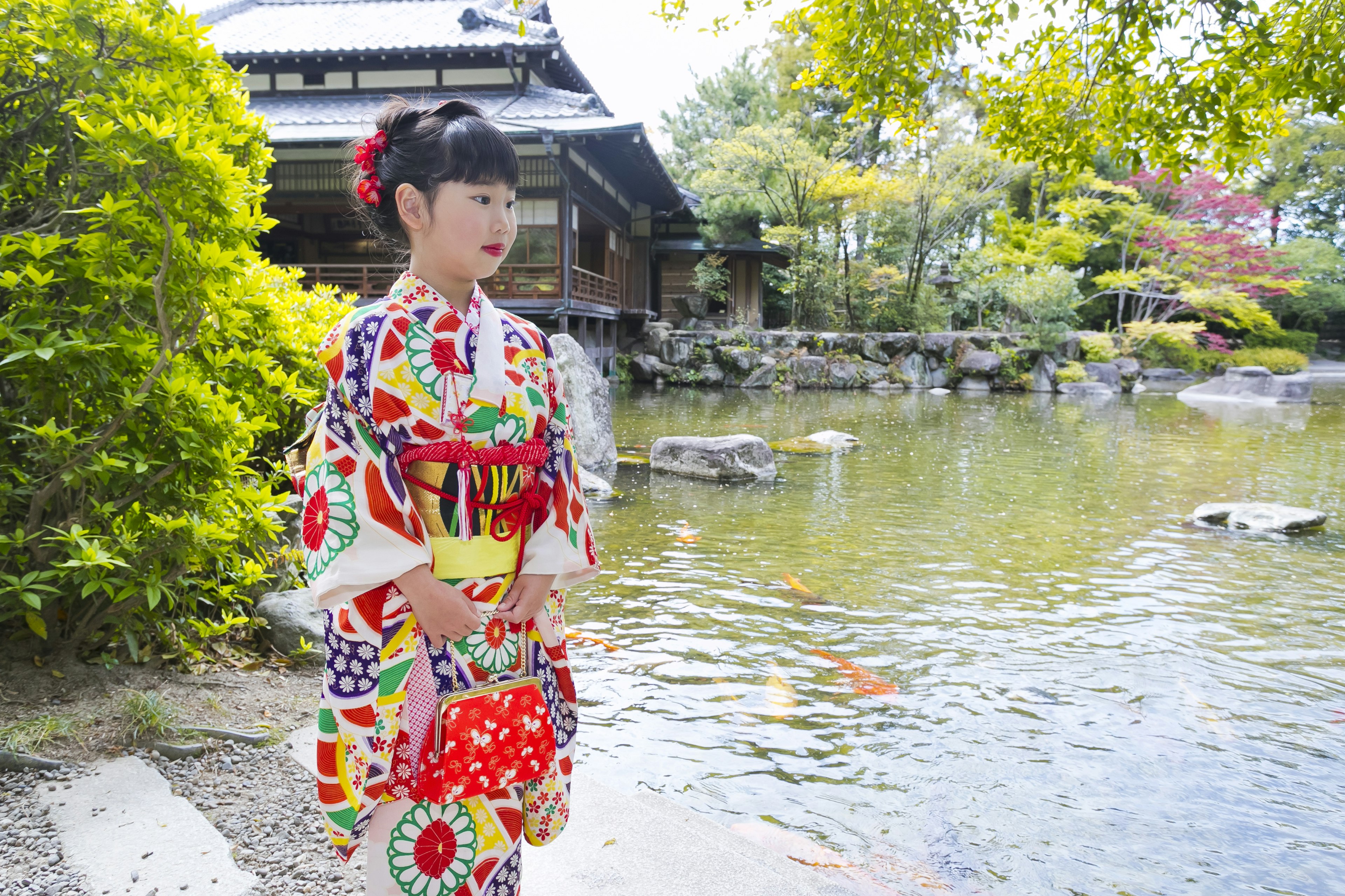 Una niña en kimono tradicional de pie junto a un estanque en un jardín