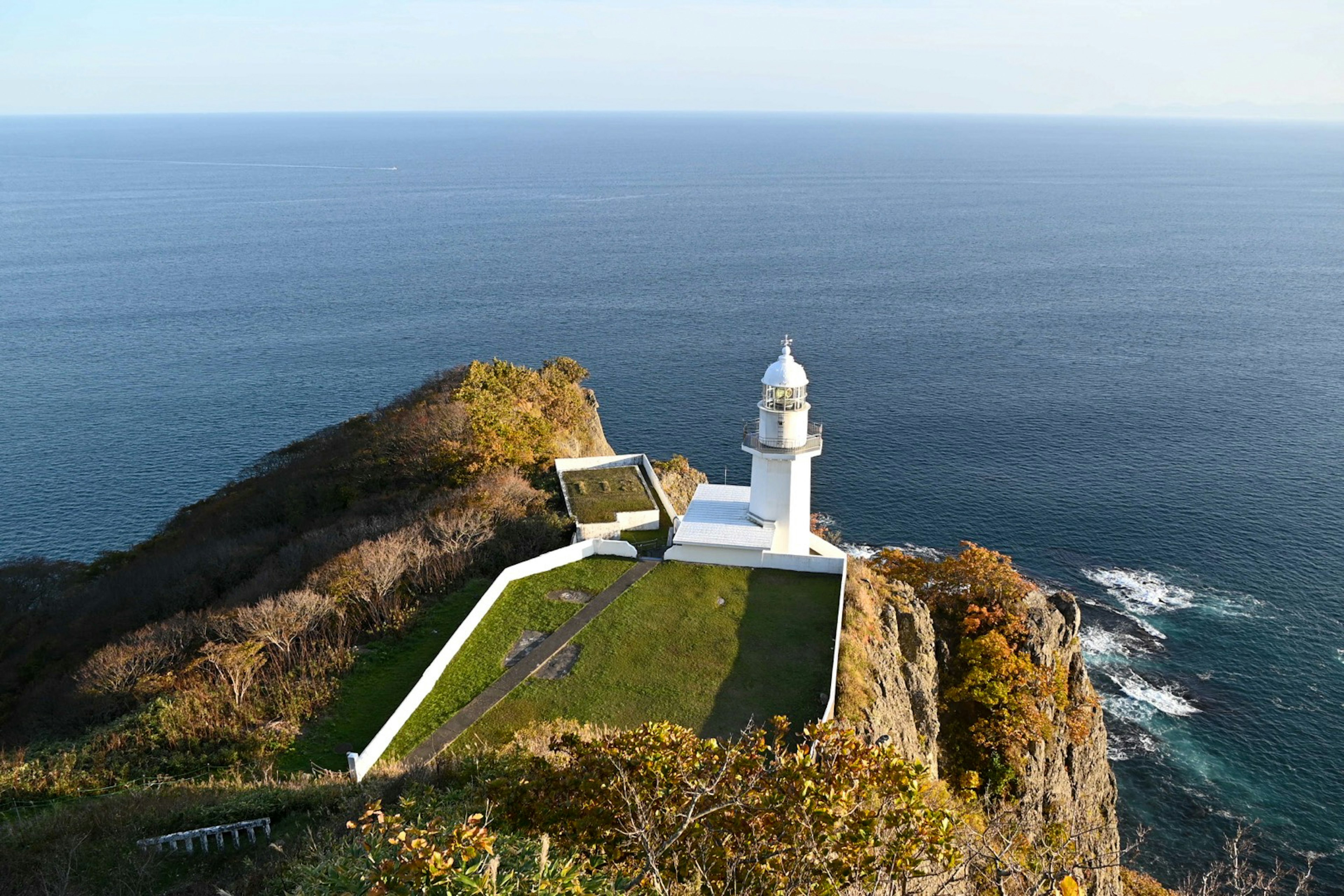 A white lighthouse with a green garden overlooking the ocean