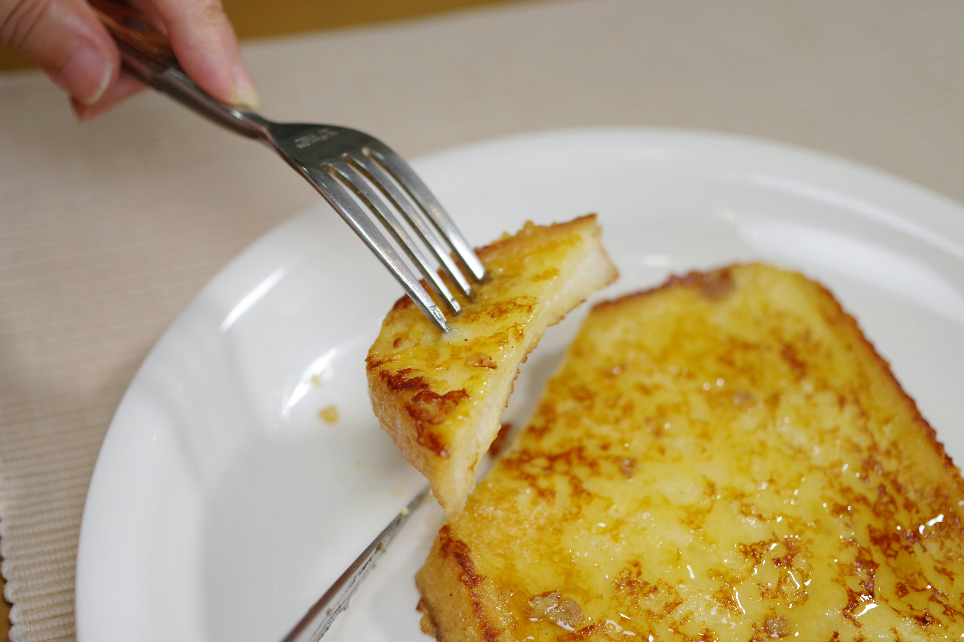 Eine Hand mit einer Gabel, die in ein Stück French Toast schneidet