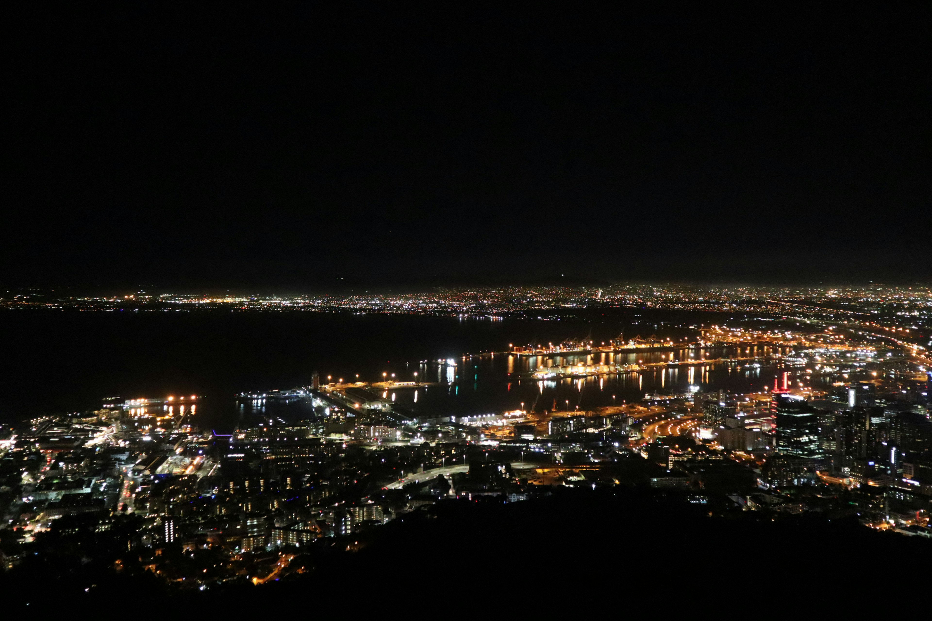 Panoramablick auf eine Stadt bei Nacht mit hellen Lichtern entlang der Küste