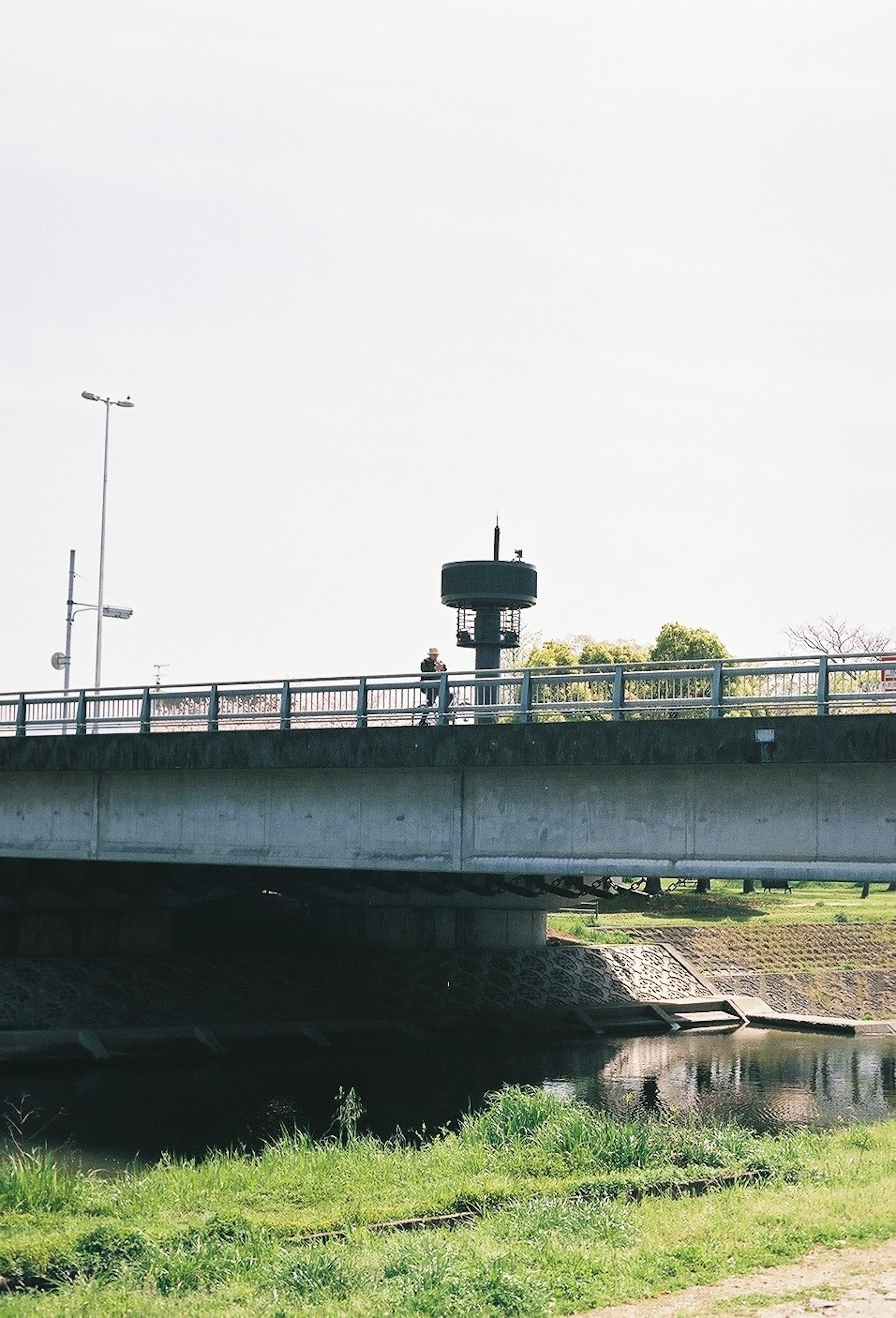 Jembatan beton di atas sungai dengan seseorang berdiri di atasnya