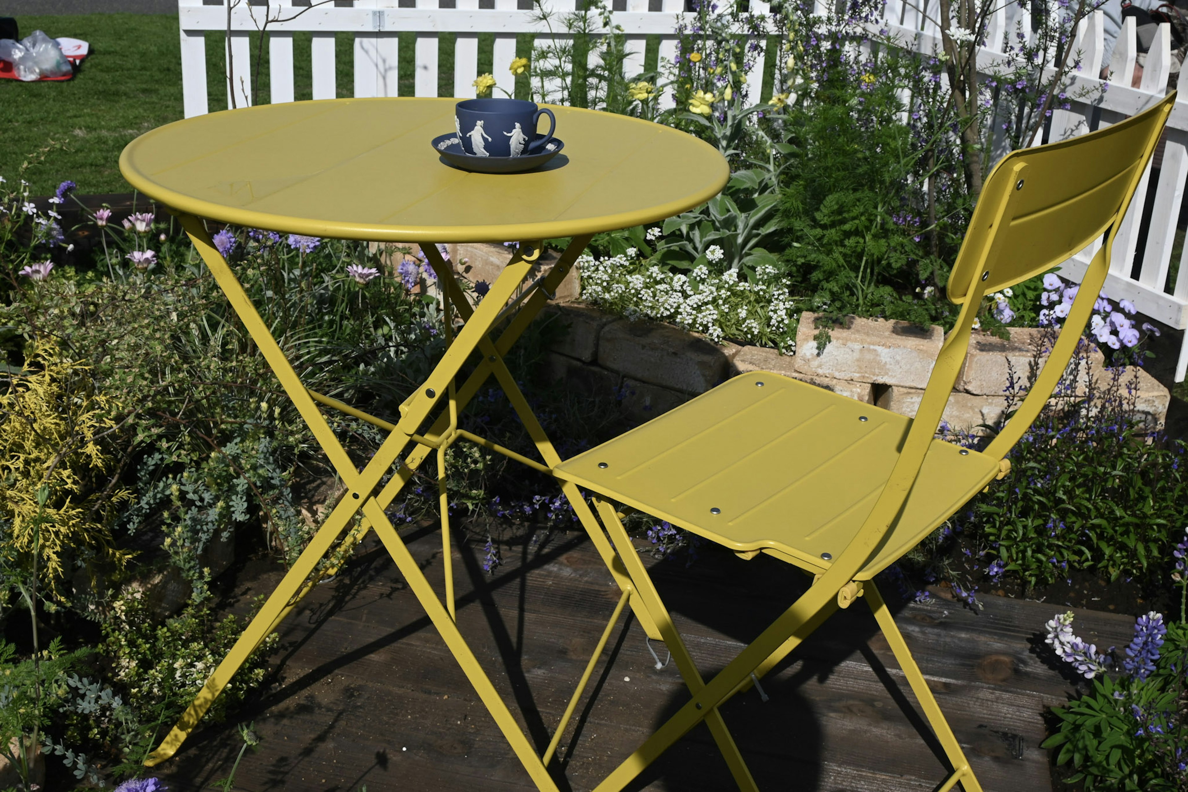 Une petite table et une chaise jaunes entourées de fleurs dans un jardin