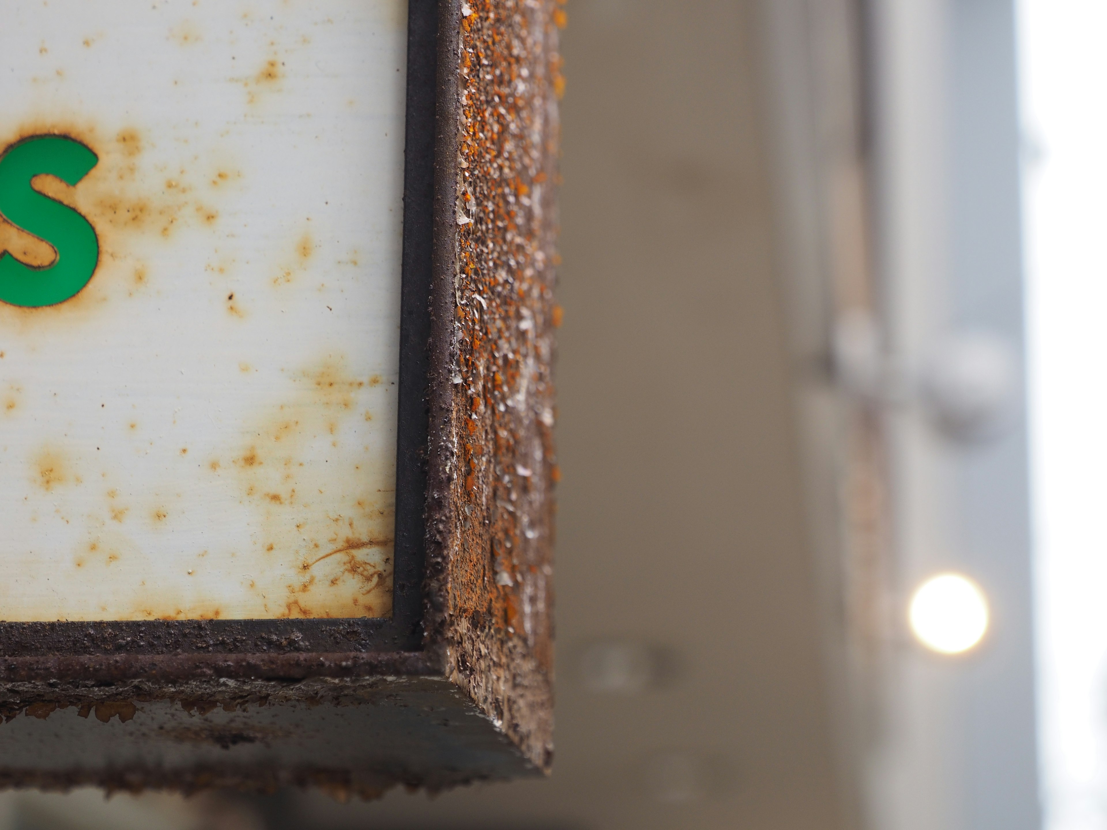 Close-up of an aged sign showing rusted metal frame and green lettering