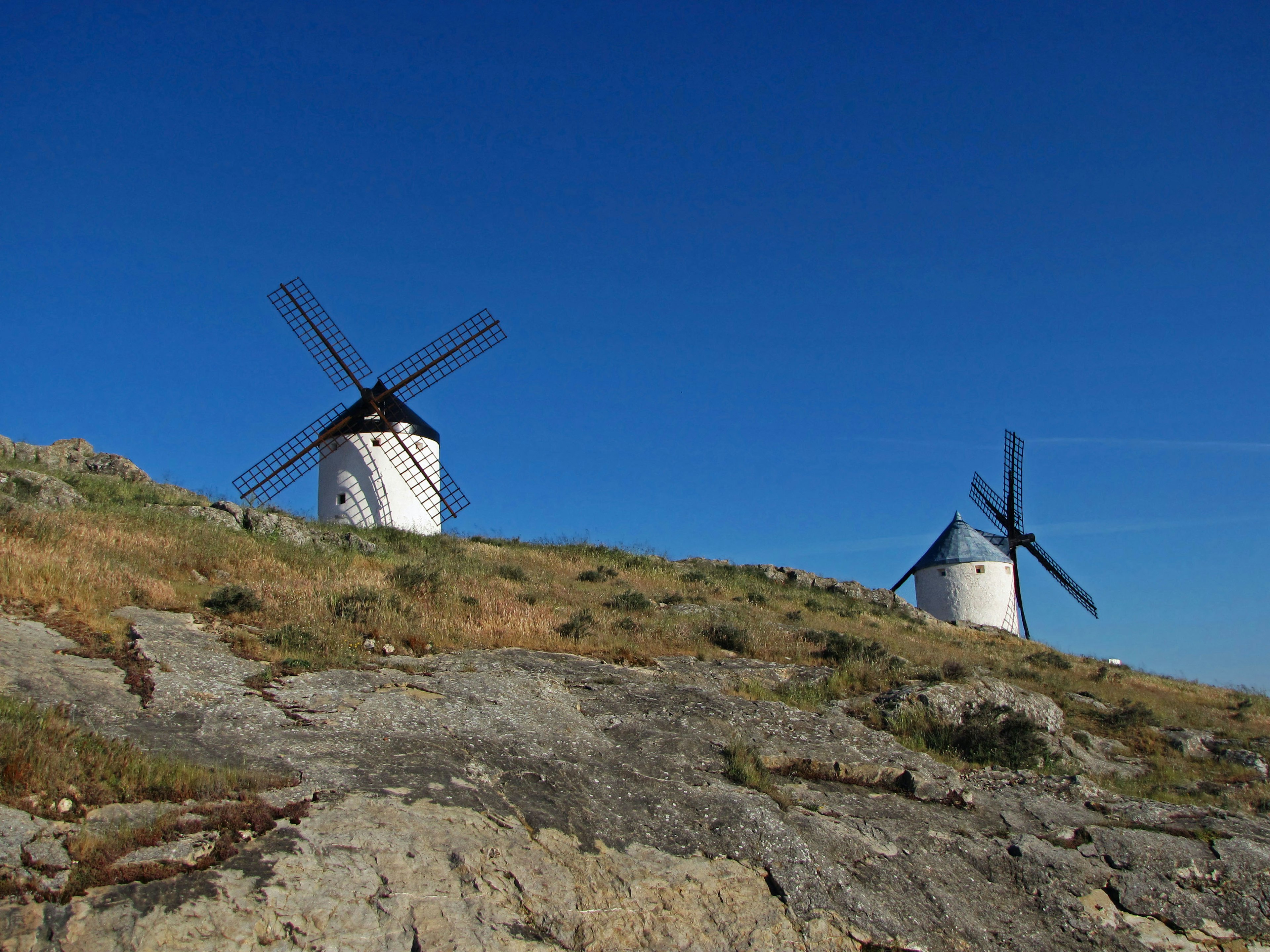 Two white windmills on a rocky hillside under a clear blue sky