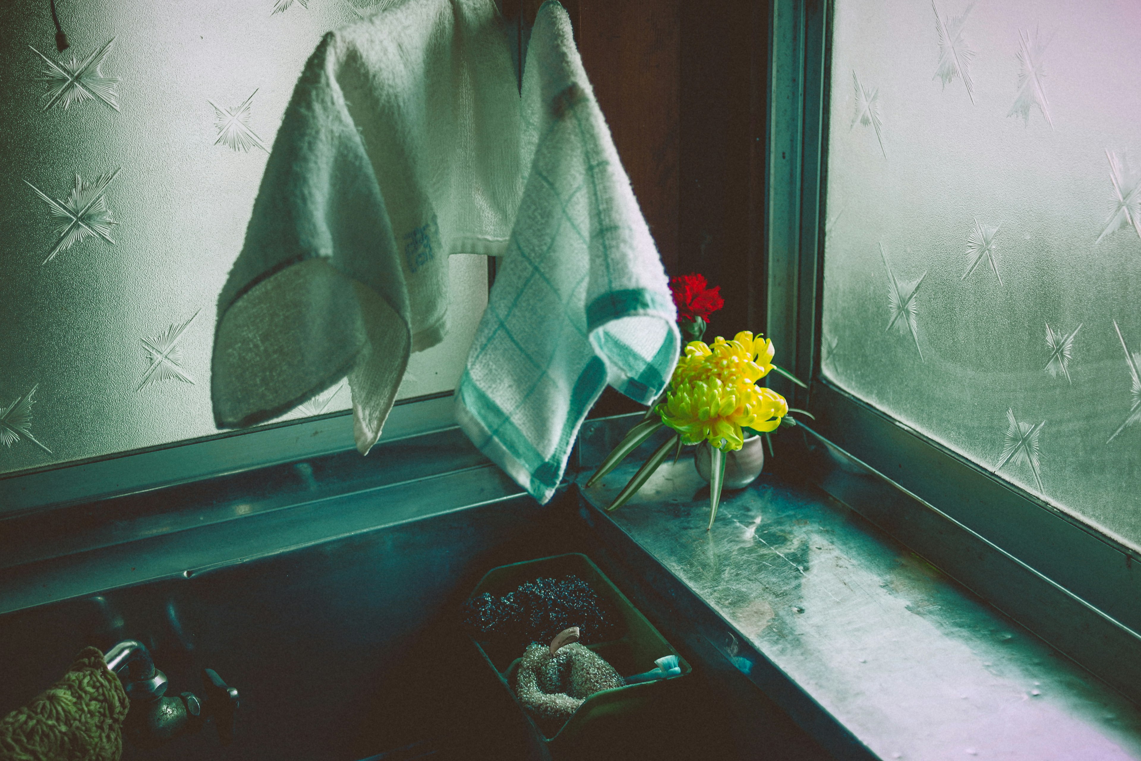 A towel hanging by a window with a vase of flowers nearby