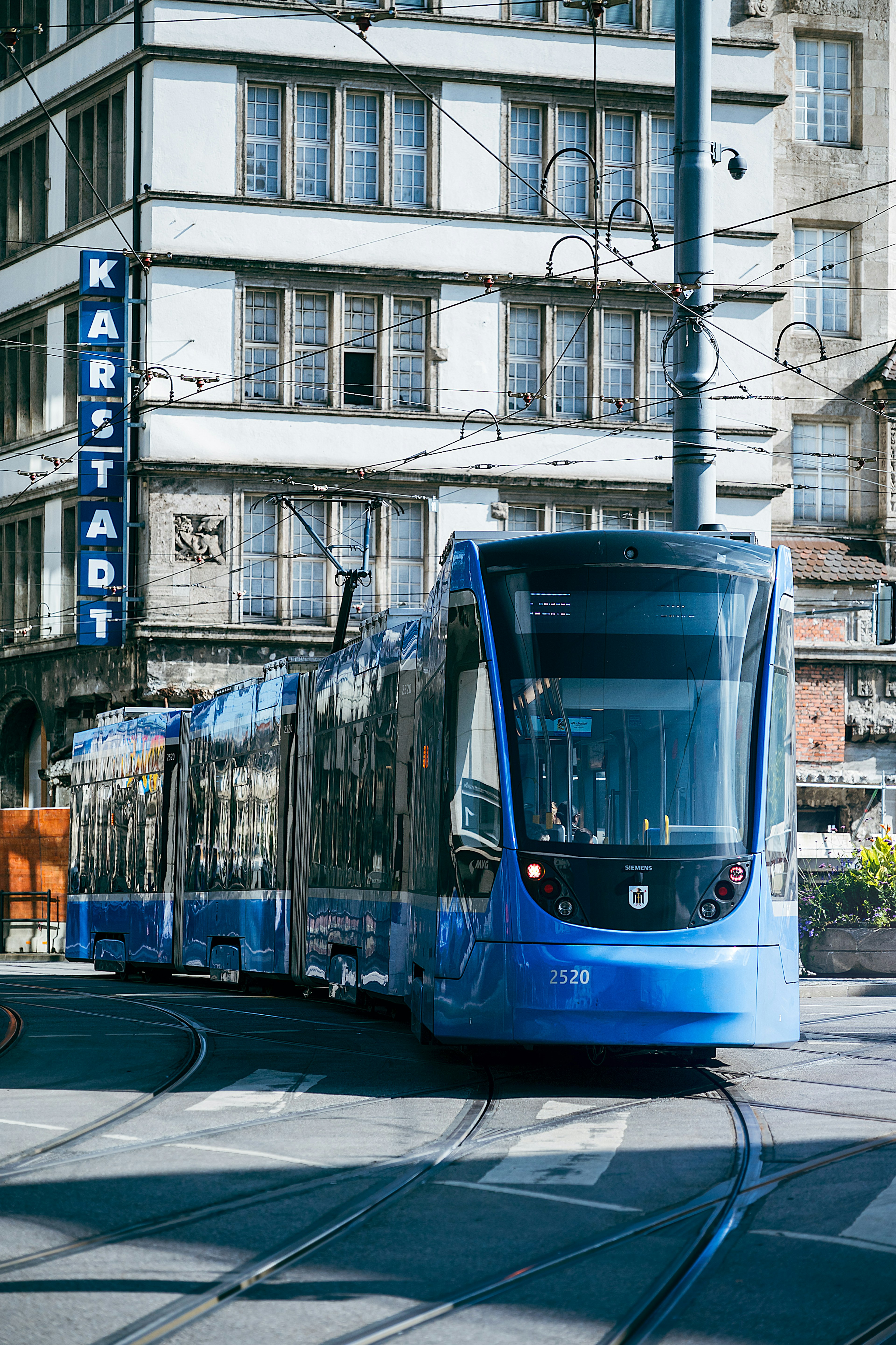 一輛藍色電車在城市中行駛，背景有卡爾施塔特的招牌