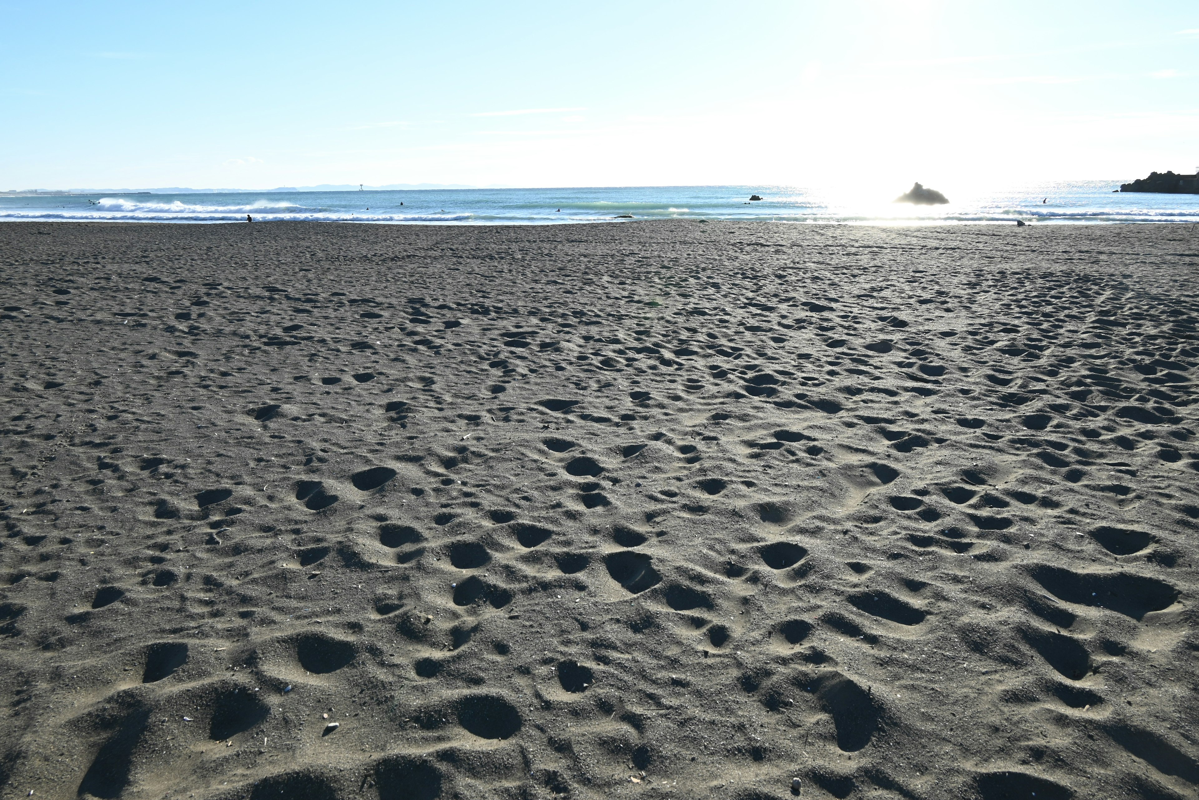 Ein Sandstrand mit verstreuten Fußabdrücken und einem blauen Meer und Himmel