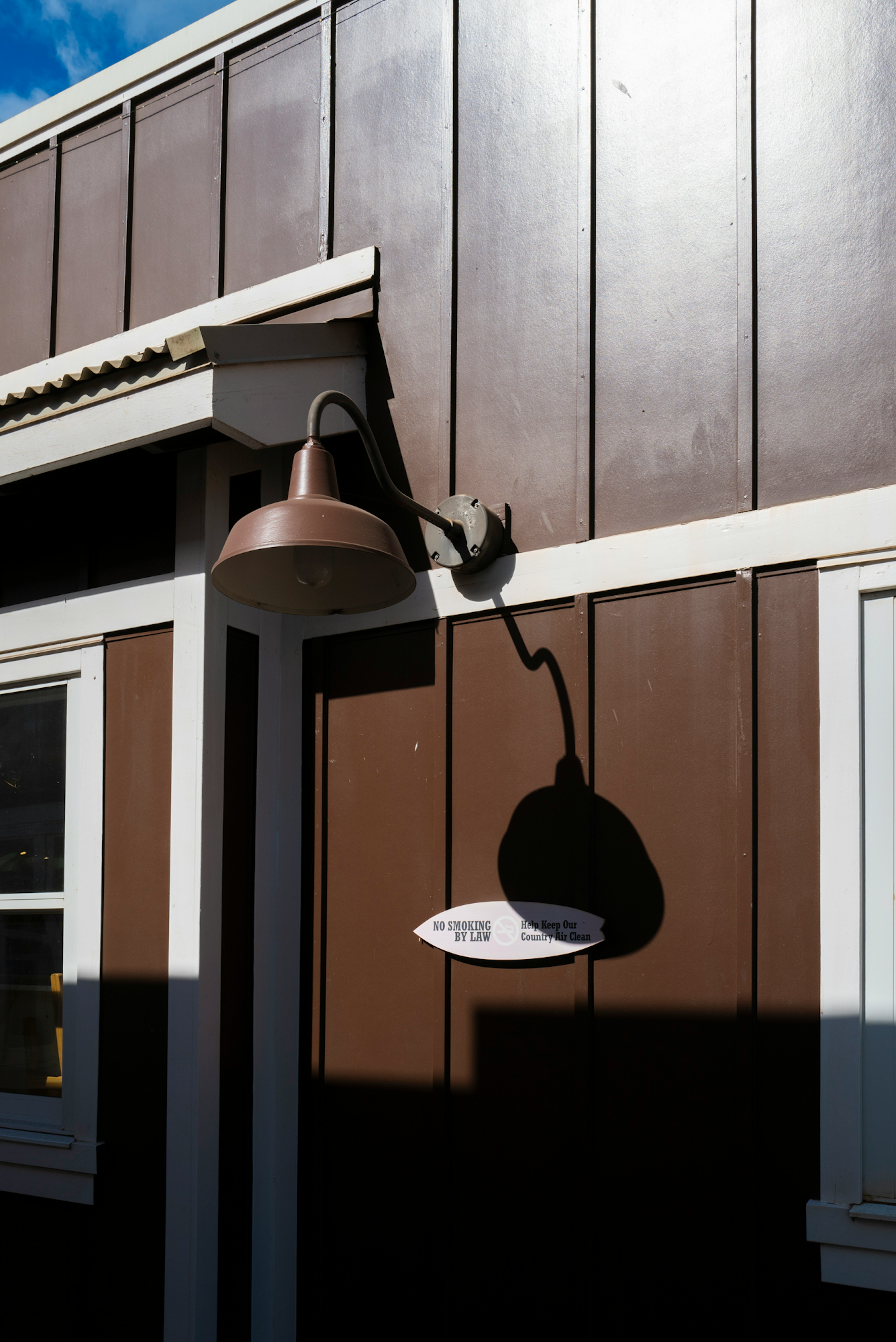 Copper light fixture attached to a brown wall casting a shadow