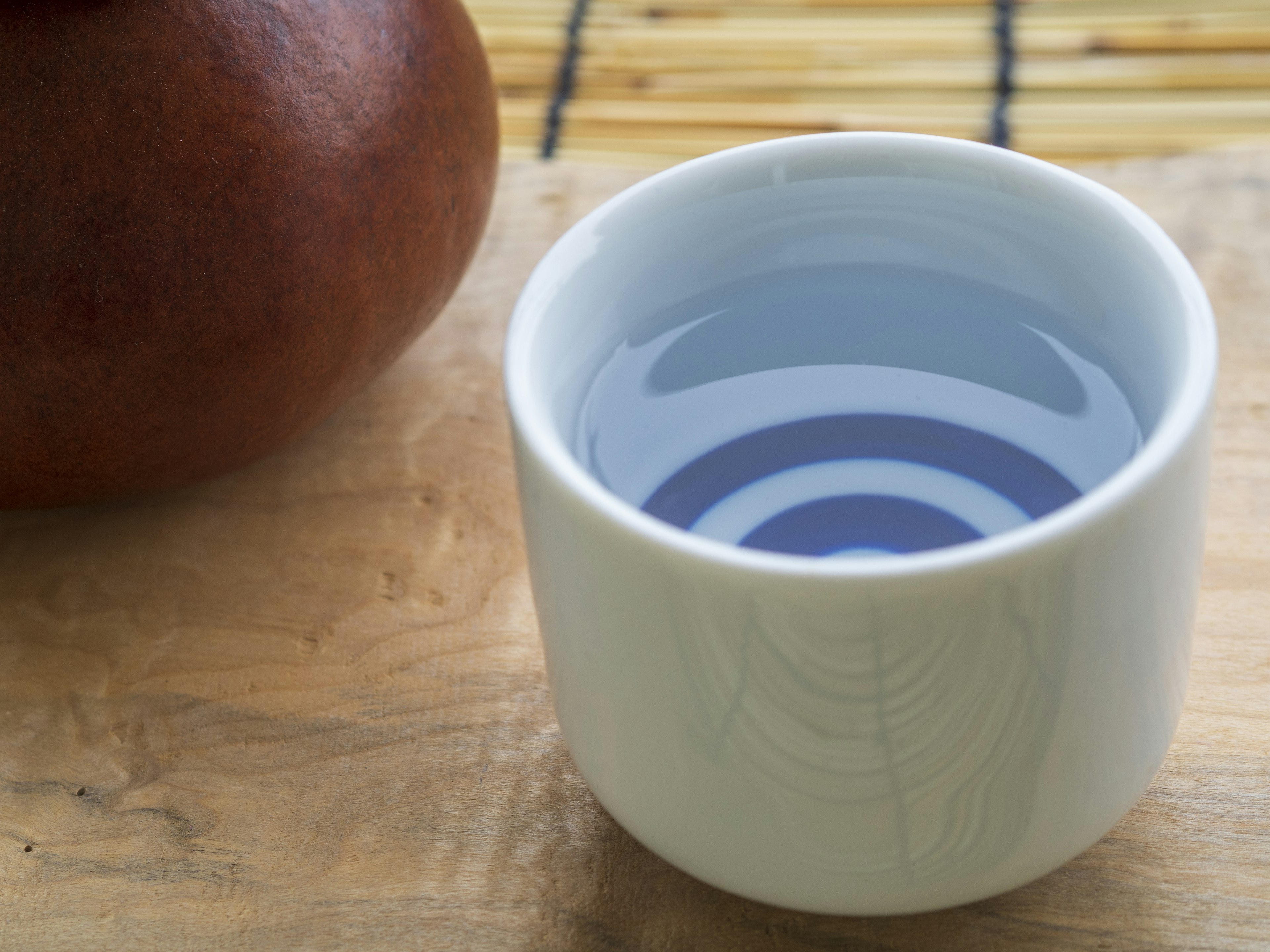 Weißer Becher mit Wasser, das Wellen erzeugt, und einem braunen Objekt im Hintergrund