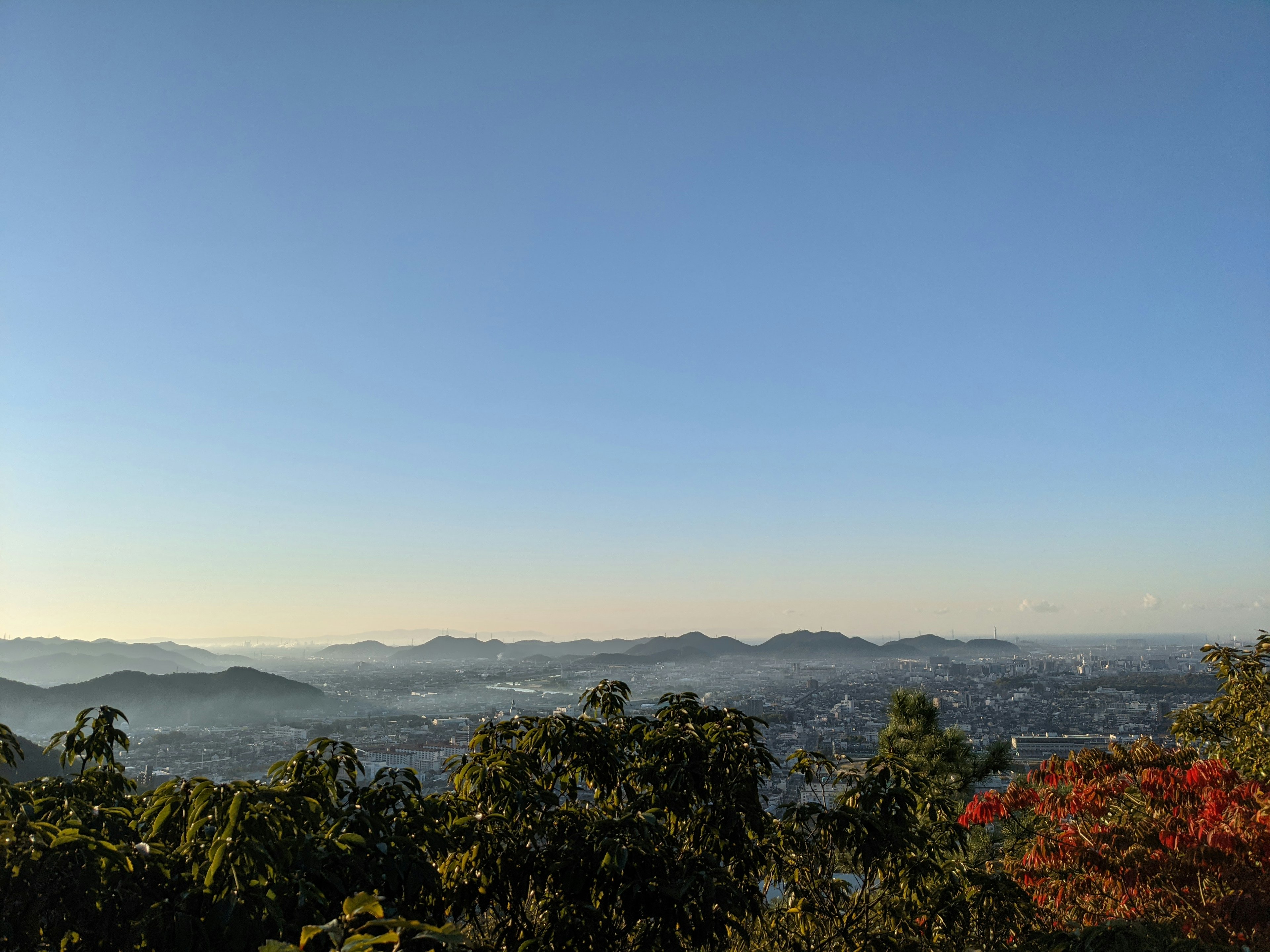 Langit biru cerah dengan latar belakang pegunungan jauh dan pemandangan kota