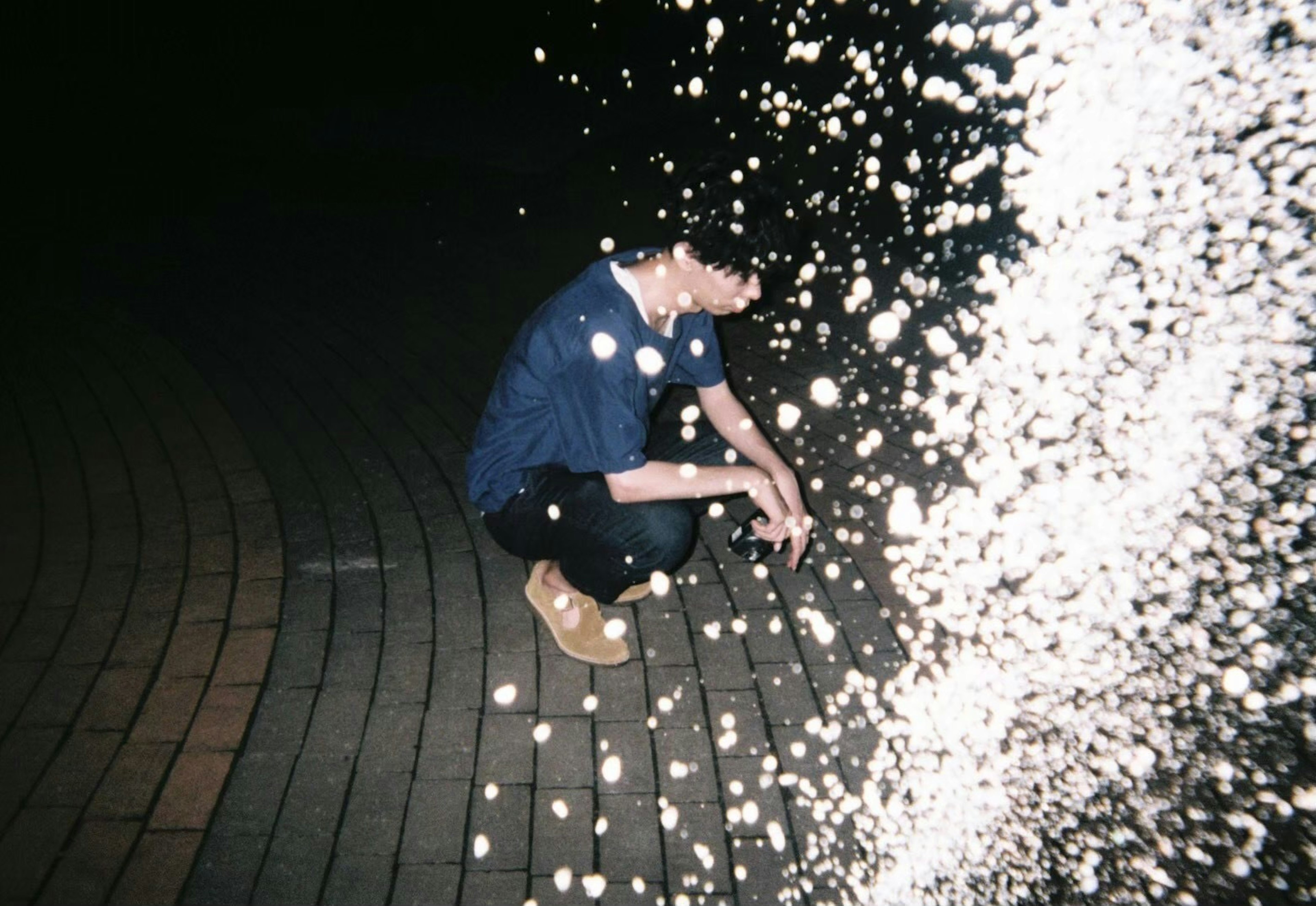 Person crouching in water spray at night in a park