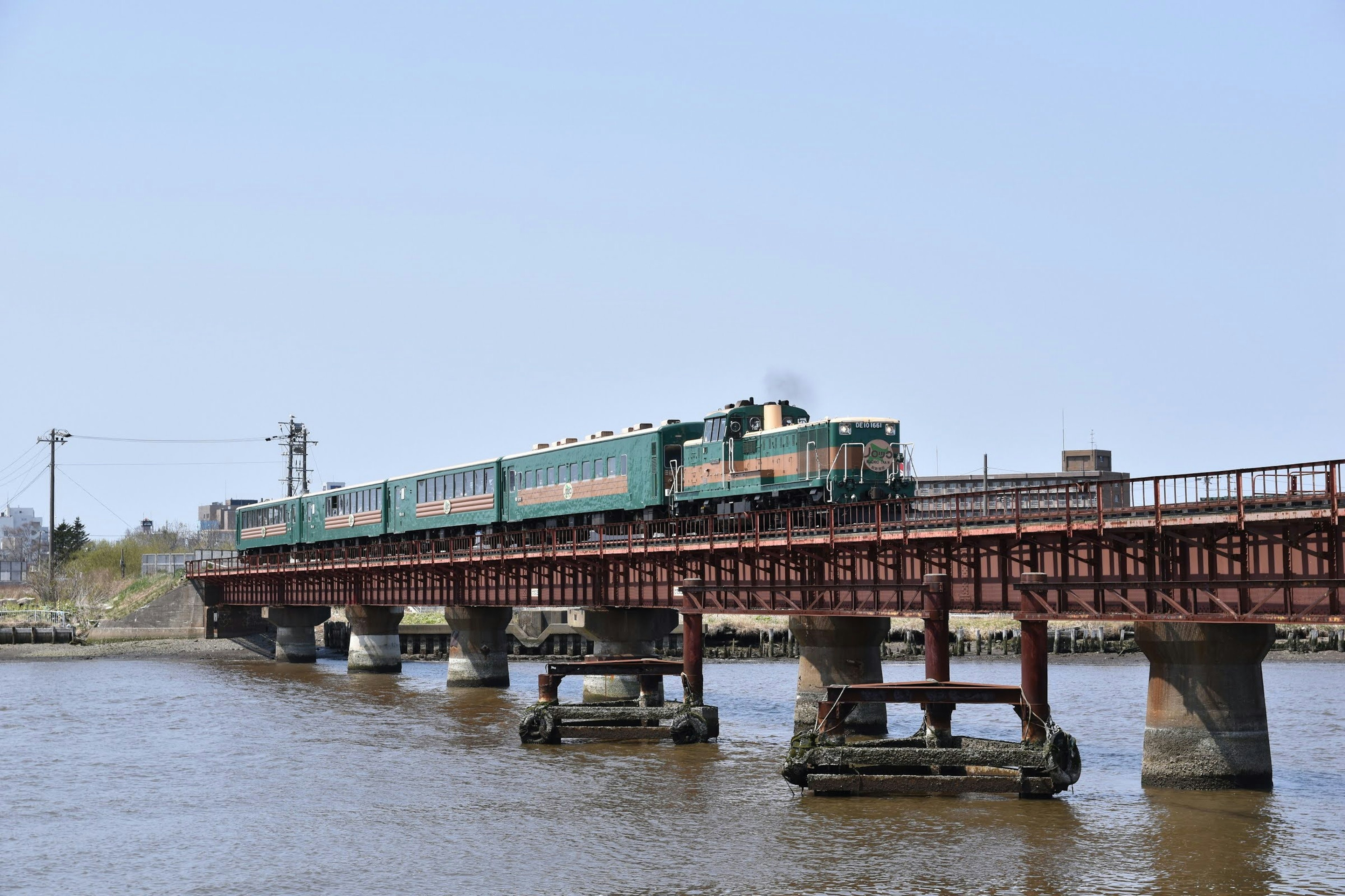 Green train crossing a bridge over a river