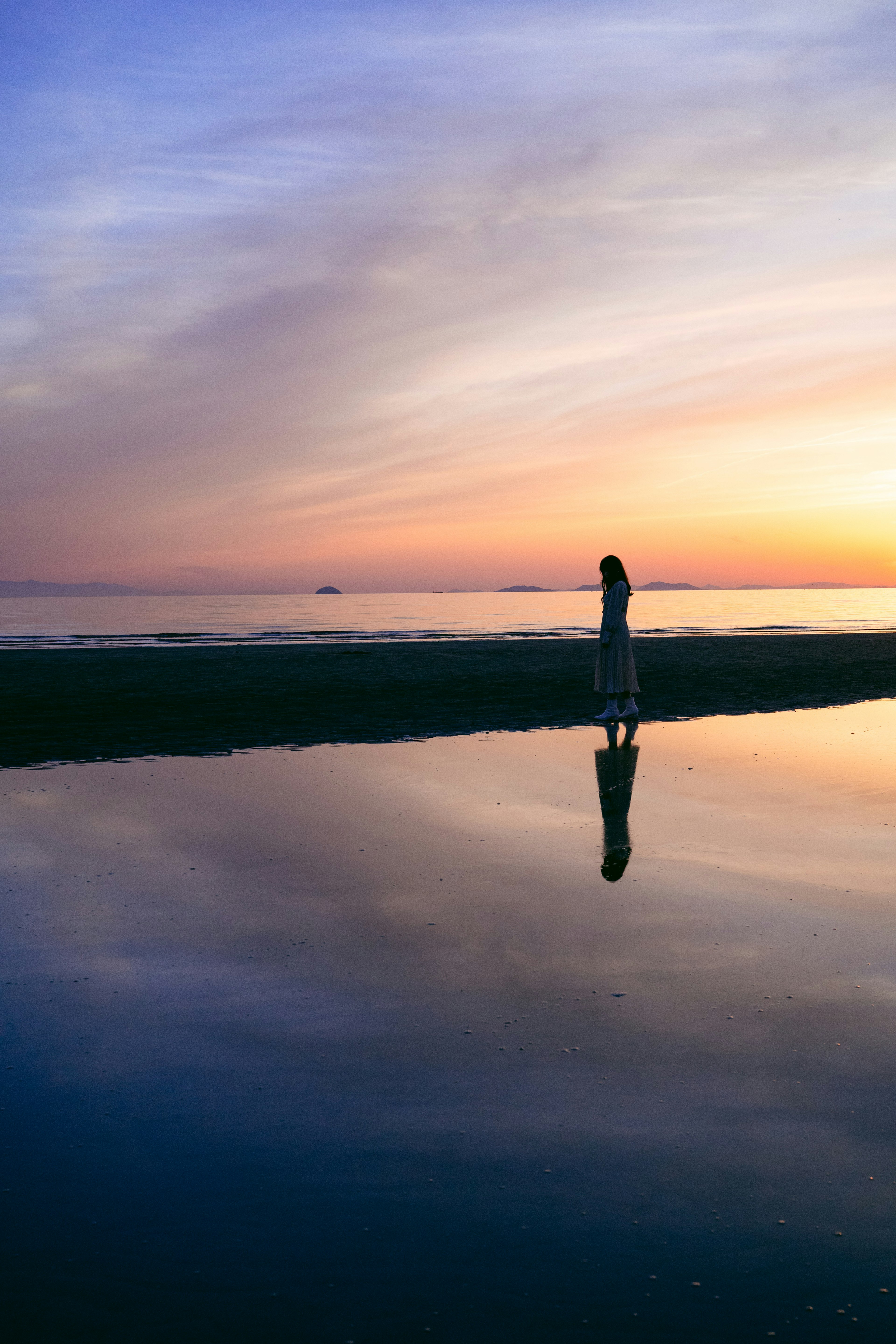 Una persona in piedi sulla spiaggia al tramonto con il riflesso visibile nell'acqua