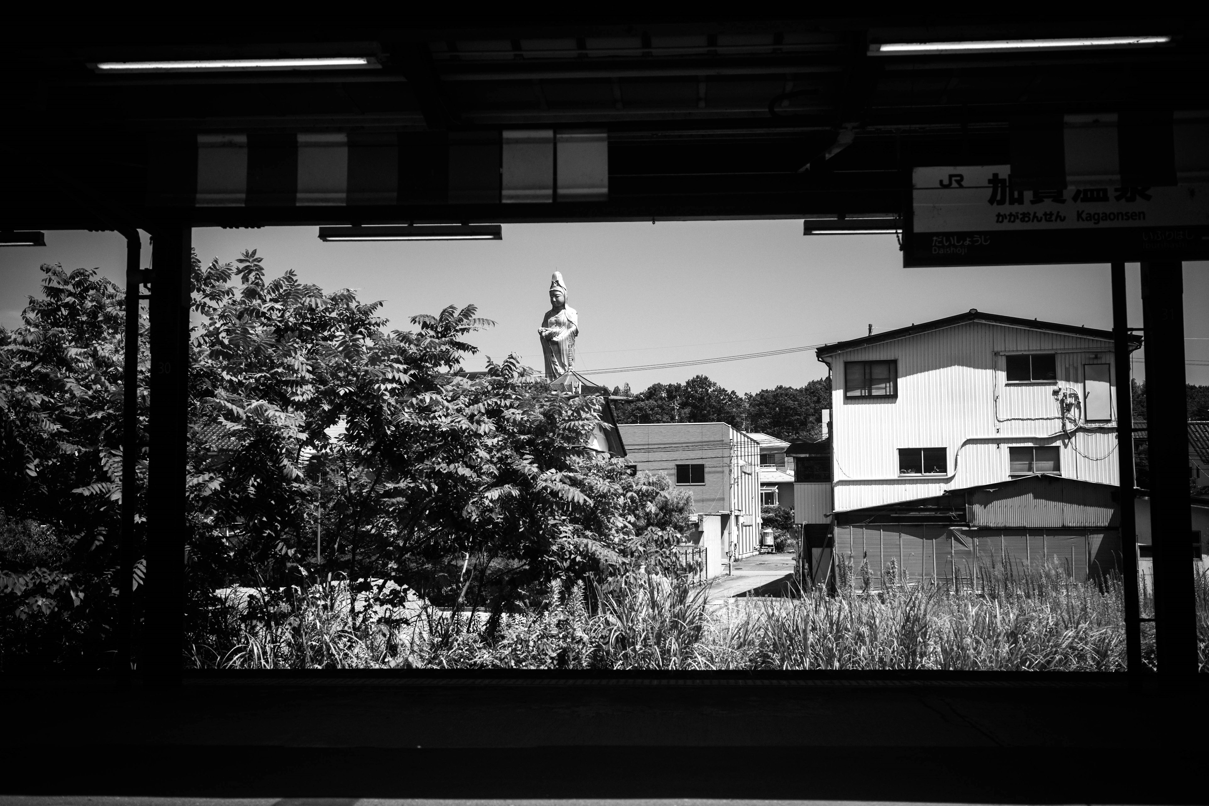 Vista en blanco y negro desde un andén de tren con una estatua y edificios circundantes