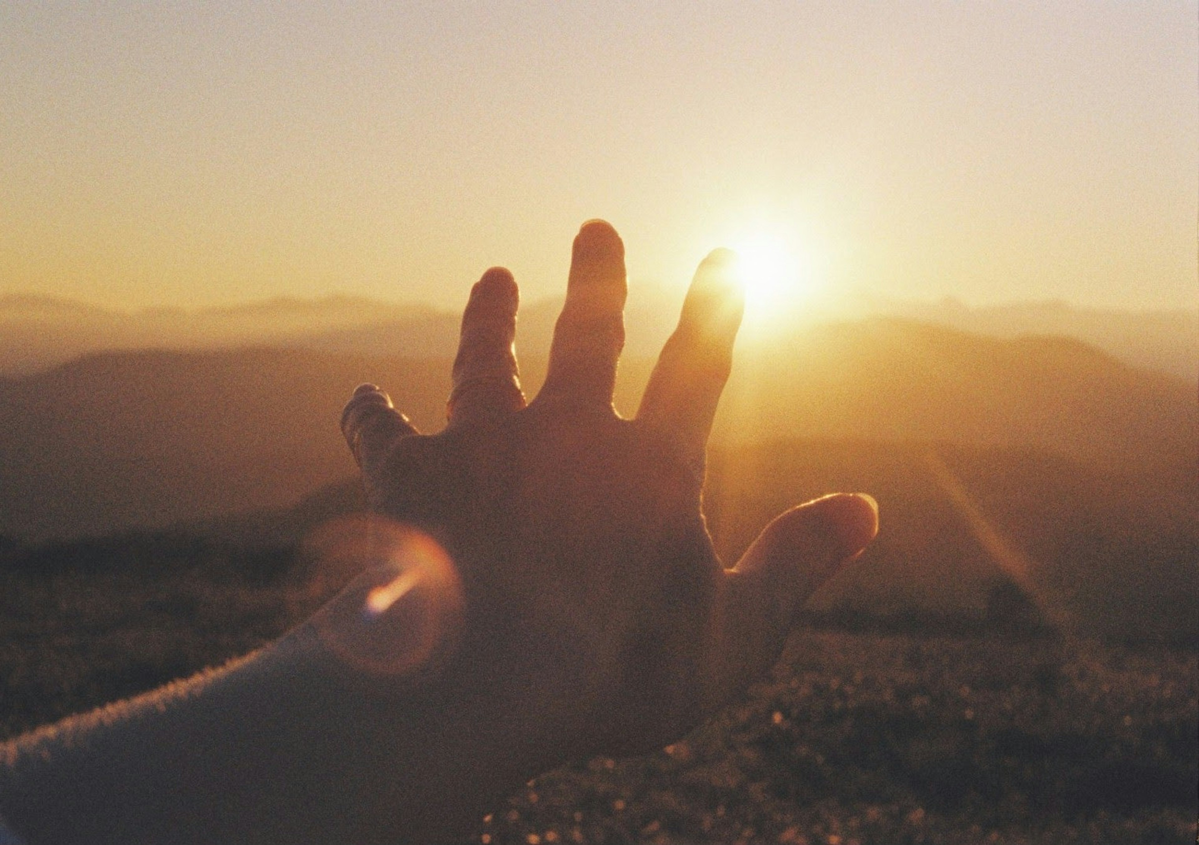 Silueta de una mano alcanzando el atardecer