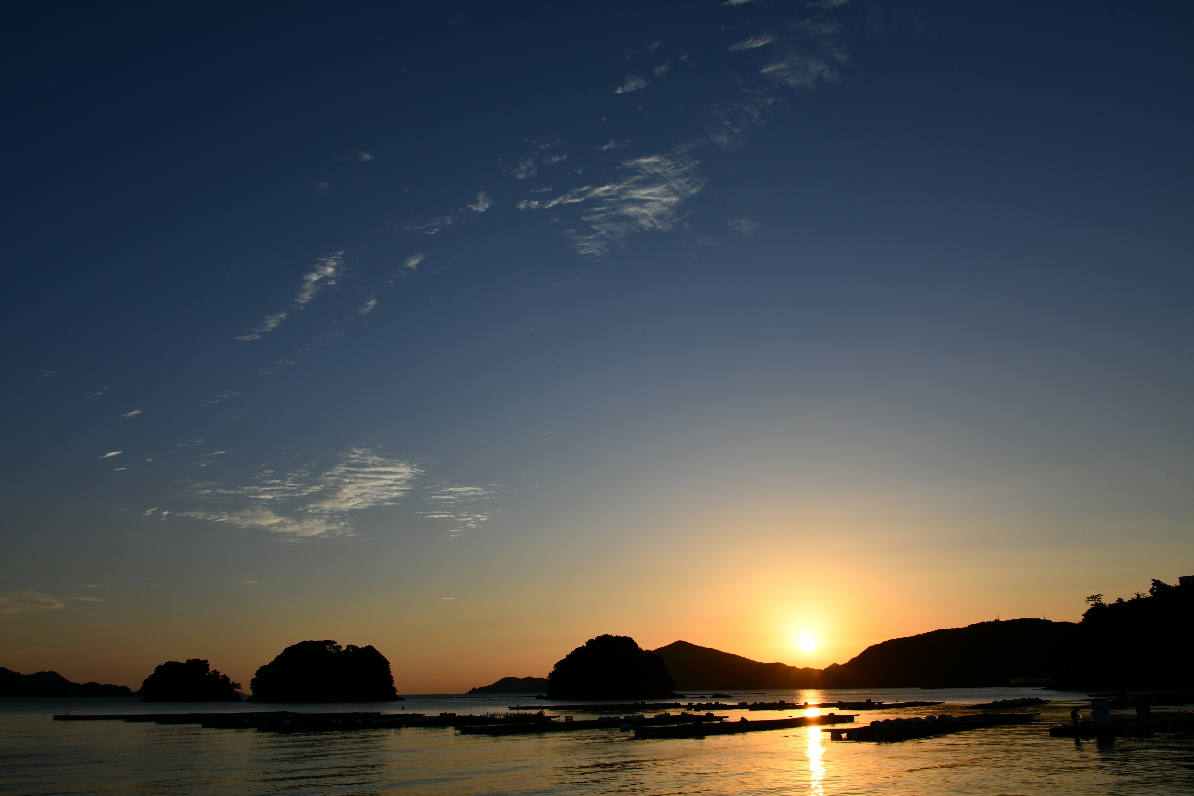 Pemandangan matahari terbenam yang indah di lautan dengan pulau-pulau siluet dan air tenang