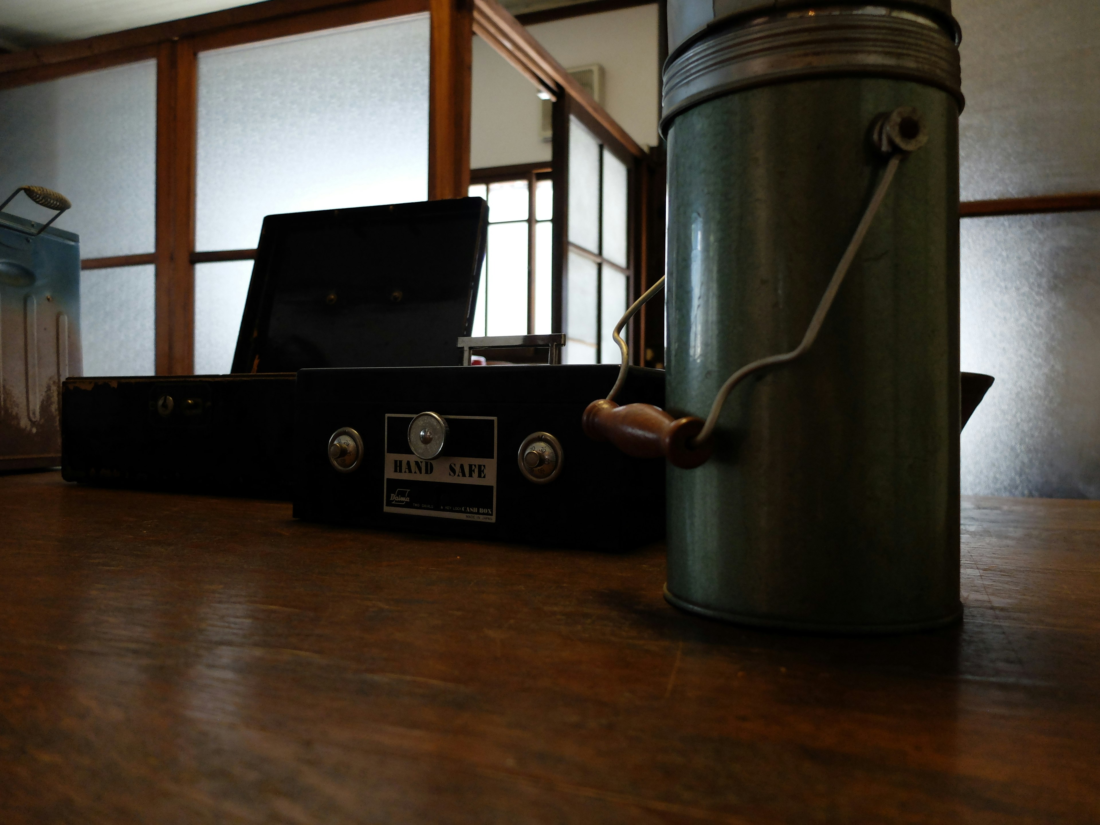 A green metal pot and a black case on a wooden table in a quiet room