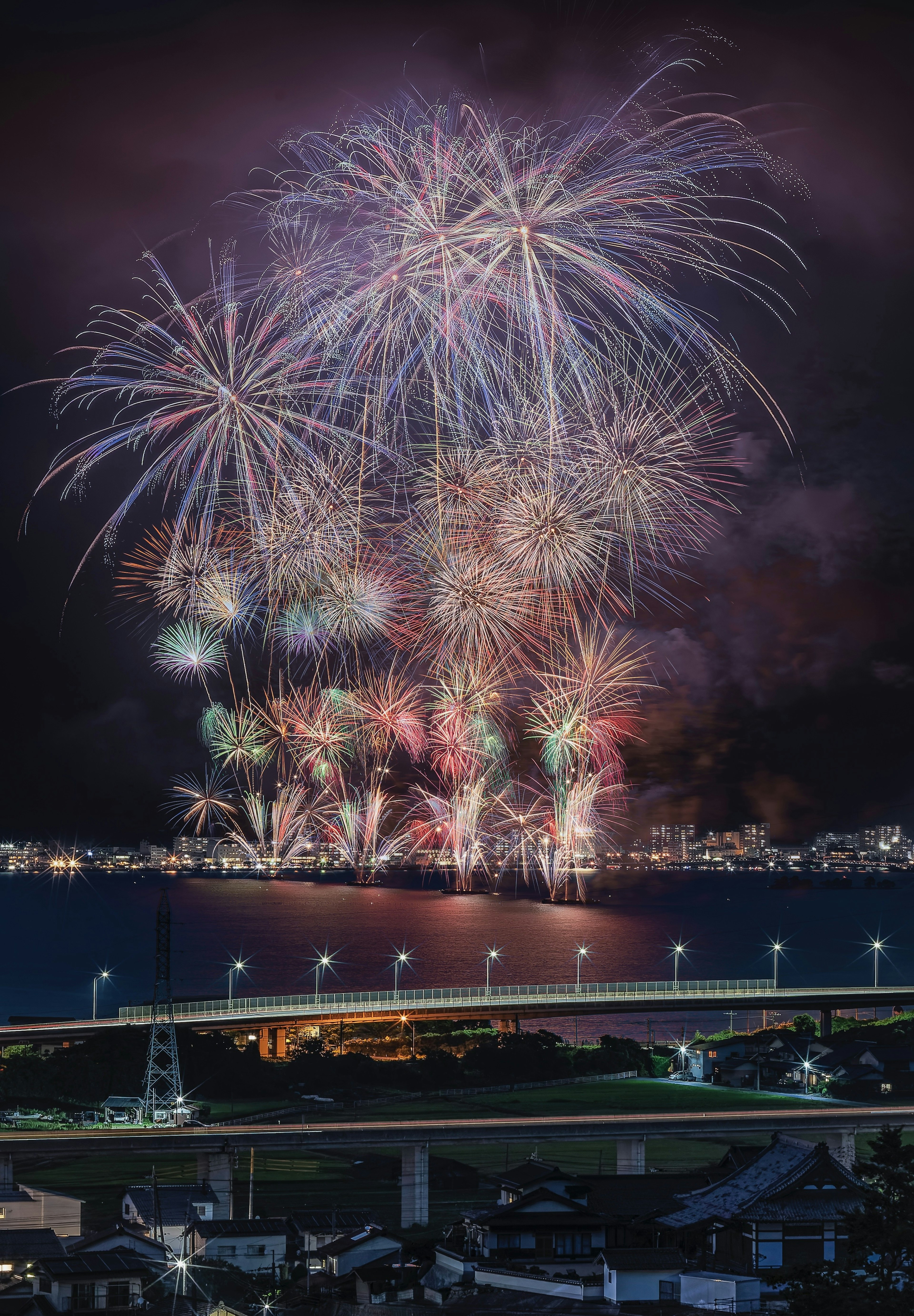 Fuochi d'artificio colorati che esplodono nel cielo notturno sopra un ponte e un paesaggio urbano