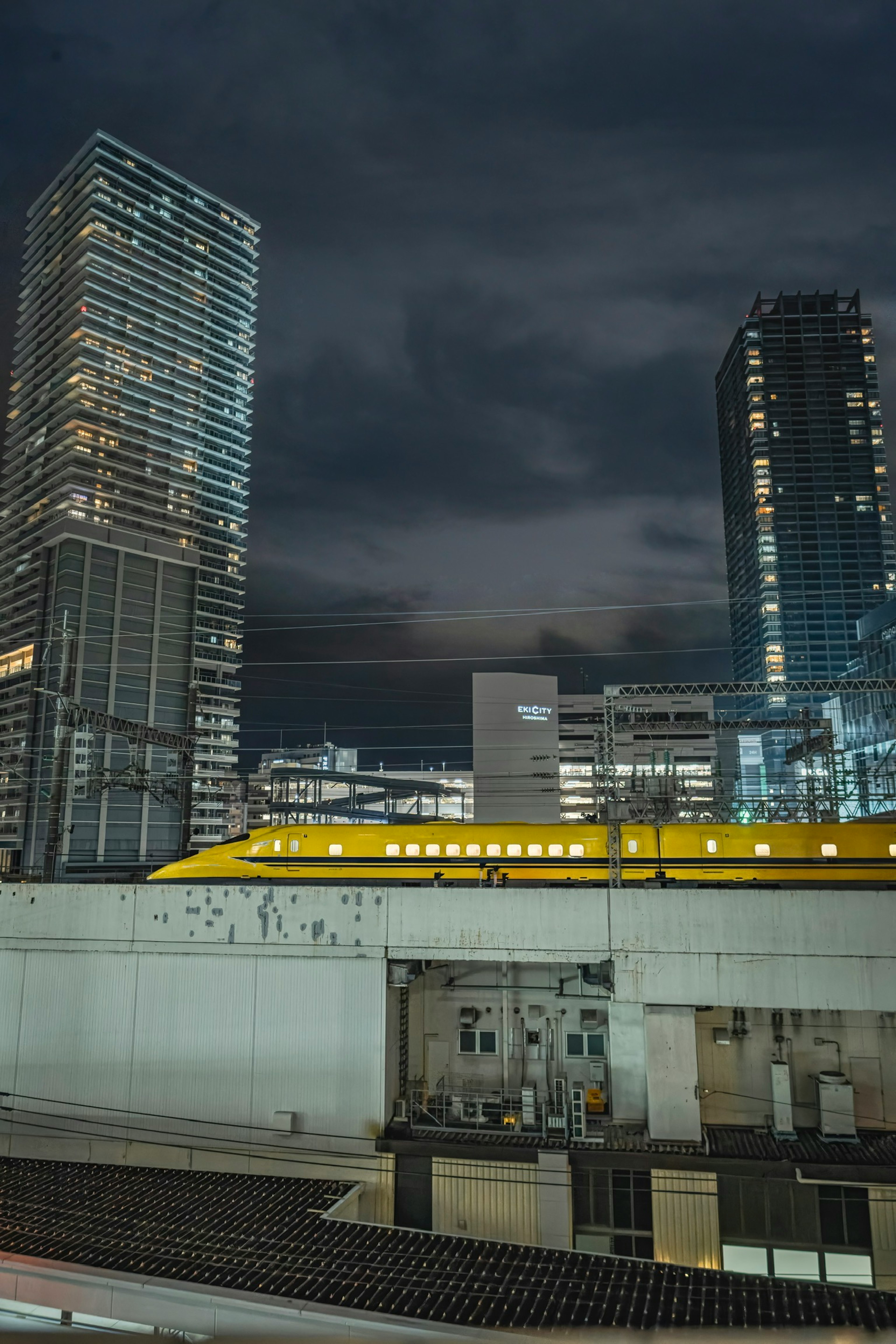 Night cityscape featuring high-rise buildings and a yellow train