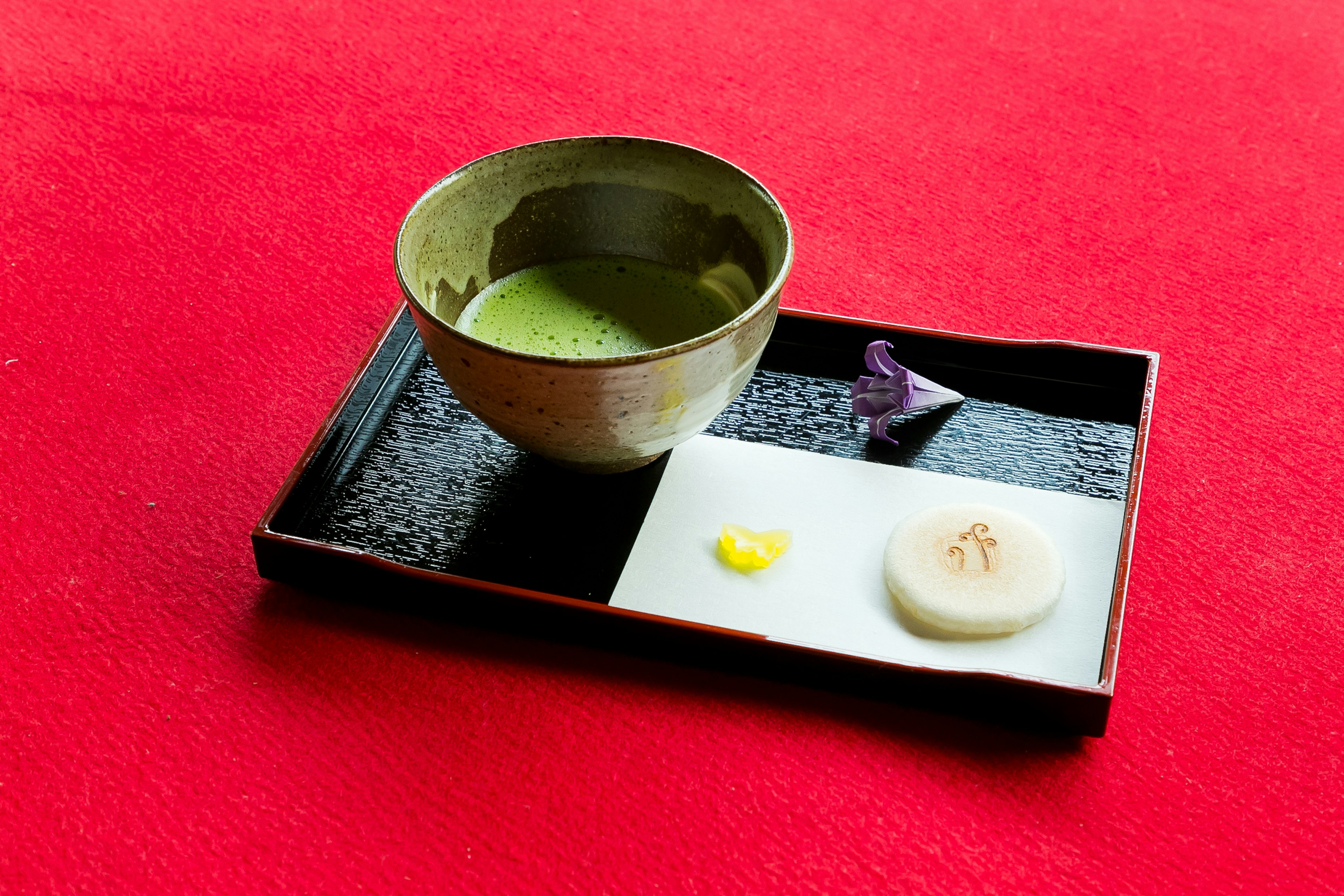 Matcha and traditional sweets on a black tray with a red background